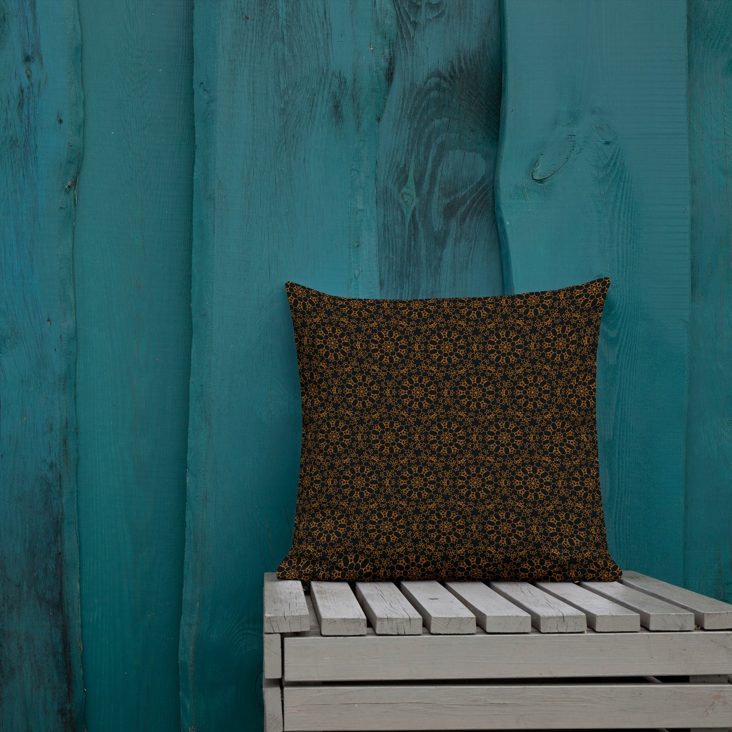 18″×18″ premium throw pillow with the 'Enneagon' black & gold geometric pattern on a wooden bench with teal wall.