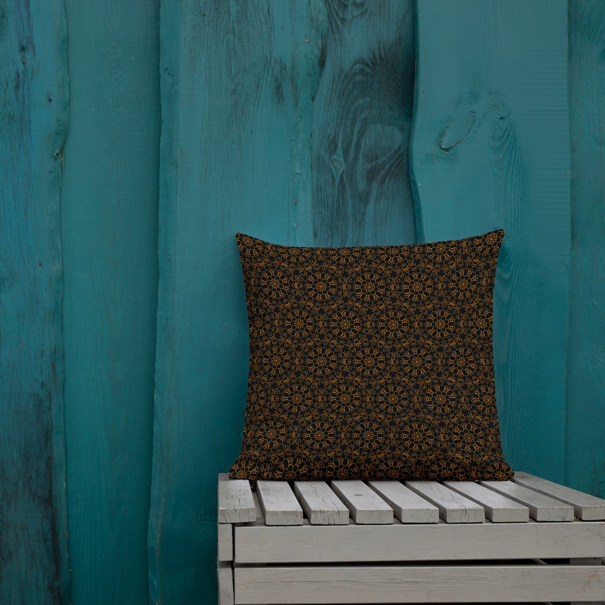 18″×18″ premium throw pillow with the 'Enneagon' black & gold geometric pattern on a wooden bench with teal wall.