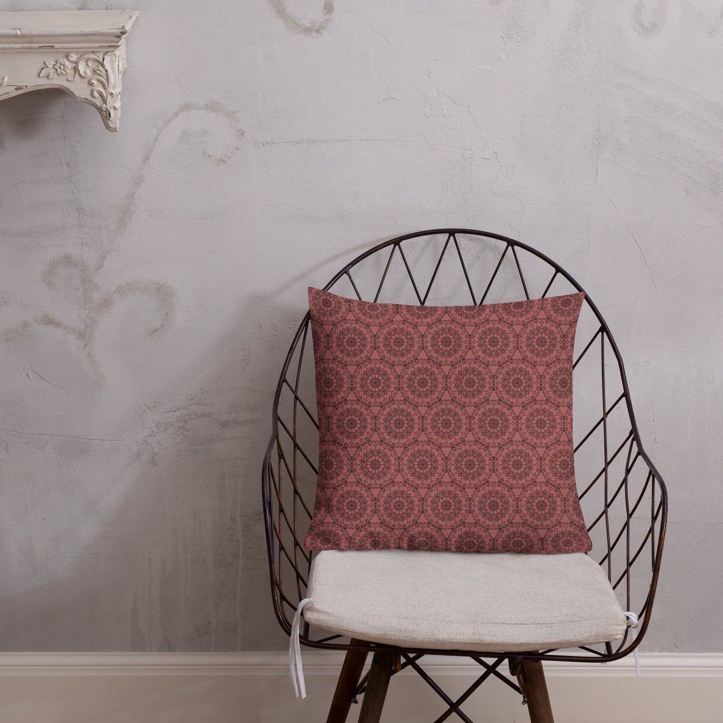 18″×18″ premium throw pillow with the 'Dodecagon' rose geometric pattern on wire chair with white cushion against textured wall.
