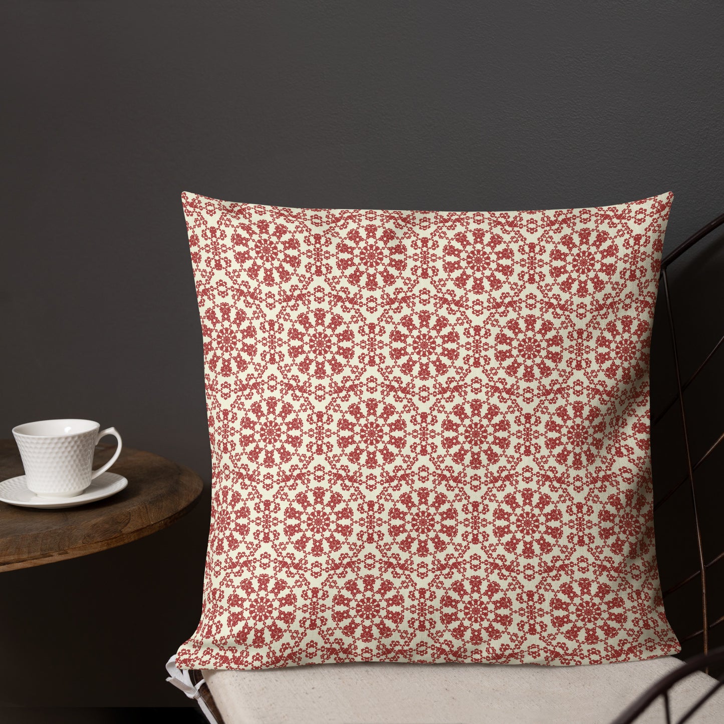 18″×18″ premium throw pillow with the ‘Decagon’ terracotta and beige geometric pattern on a dark chair with a coffee cup on a side table.