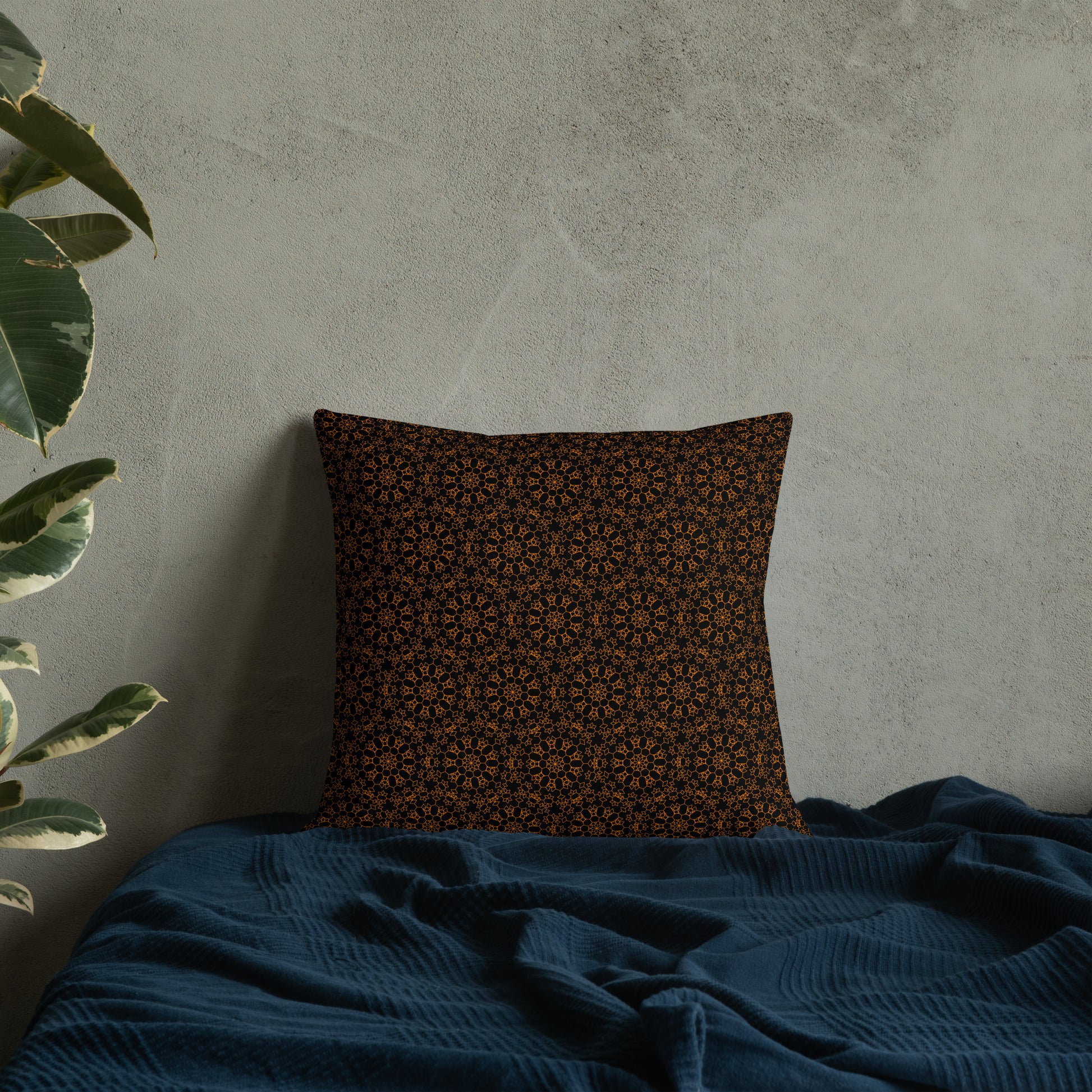 18″×18″ premium throw pillow with the 'Enneagon' black & gold geometric pattern on a bed with dark teal blanket.