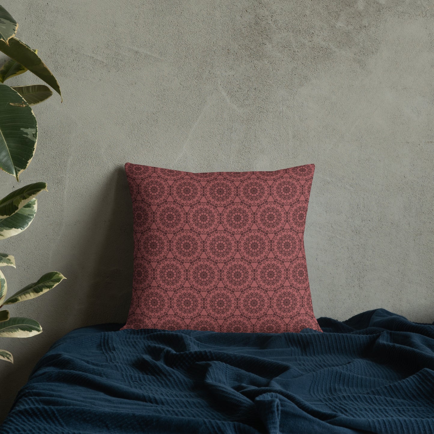 18″×18″ premium throw pillow with the 'Dodecagon' rose geometric pattern on bed with dark teal blanket against concrete wall.