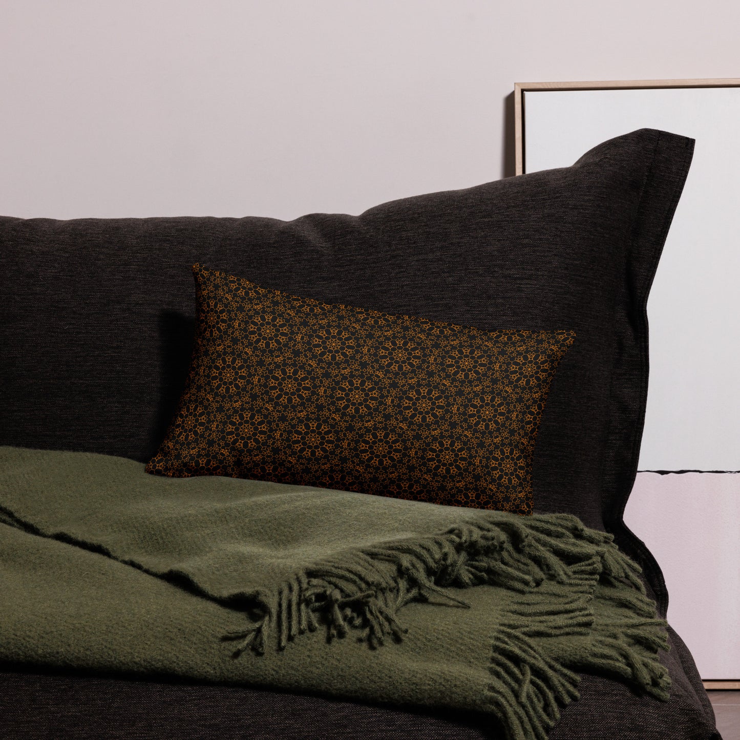 20″×12″ premium throw pillow with the 'Enneagon' black & gold geometric pattern on a dark sofa with green throw blanket.