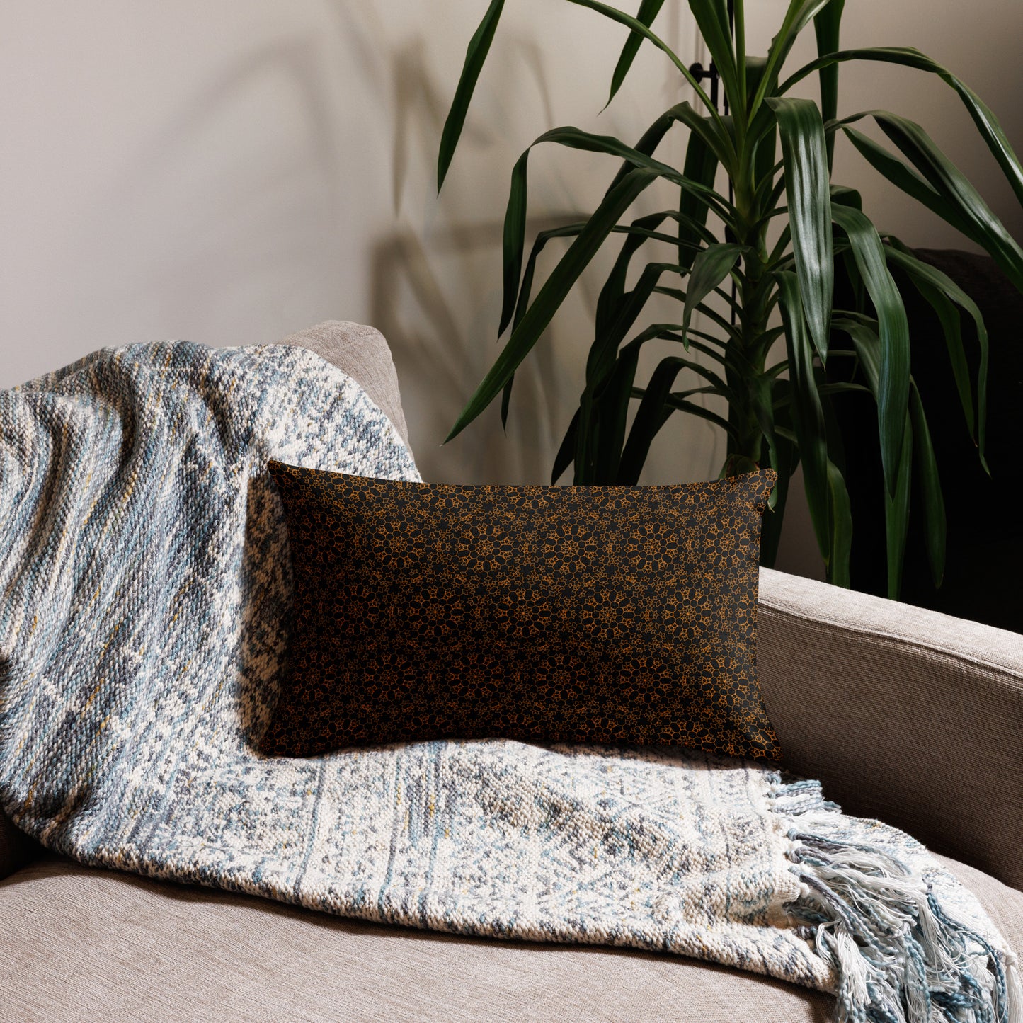 20″×12″ premium throw pillow with the 'Enneagon' black & gold geometric pattern on a sofa with textured throw blanket.