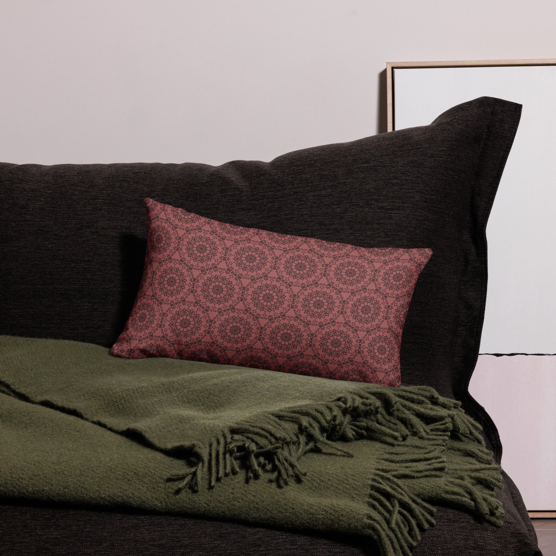 20″×12″ premium throw pillow with the 'Dodecagon' rose geometric pattern on dark sofa with green fringed throw.