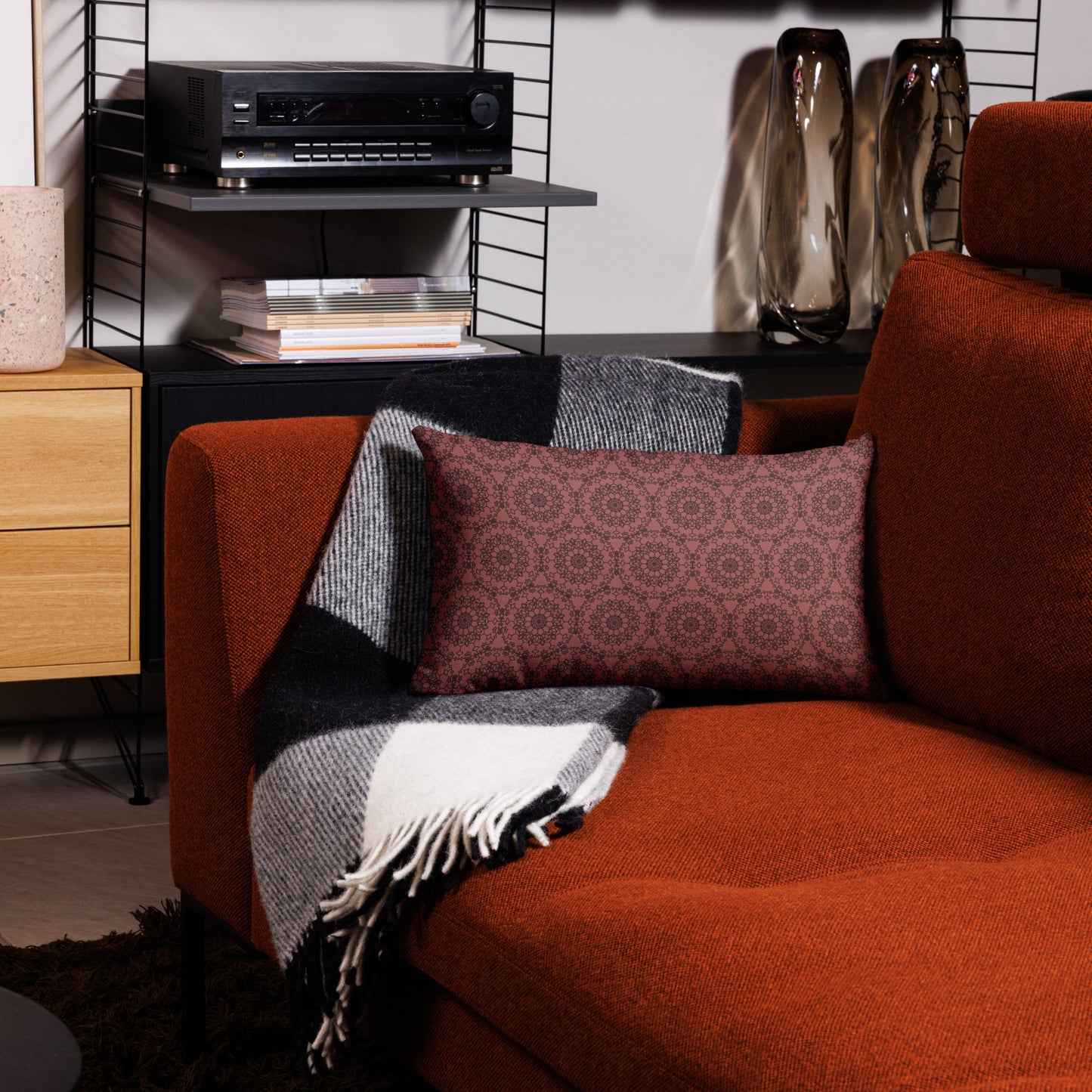 20″×12″ premium throw pillow with the 'Dodecagon' rose geometric pattern on orange armchair with checkered blanket.