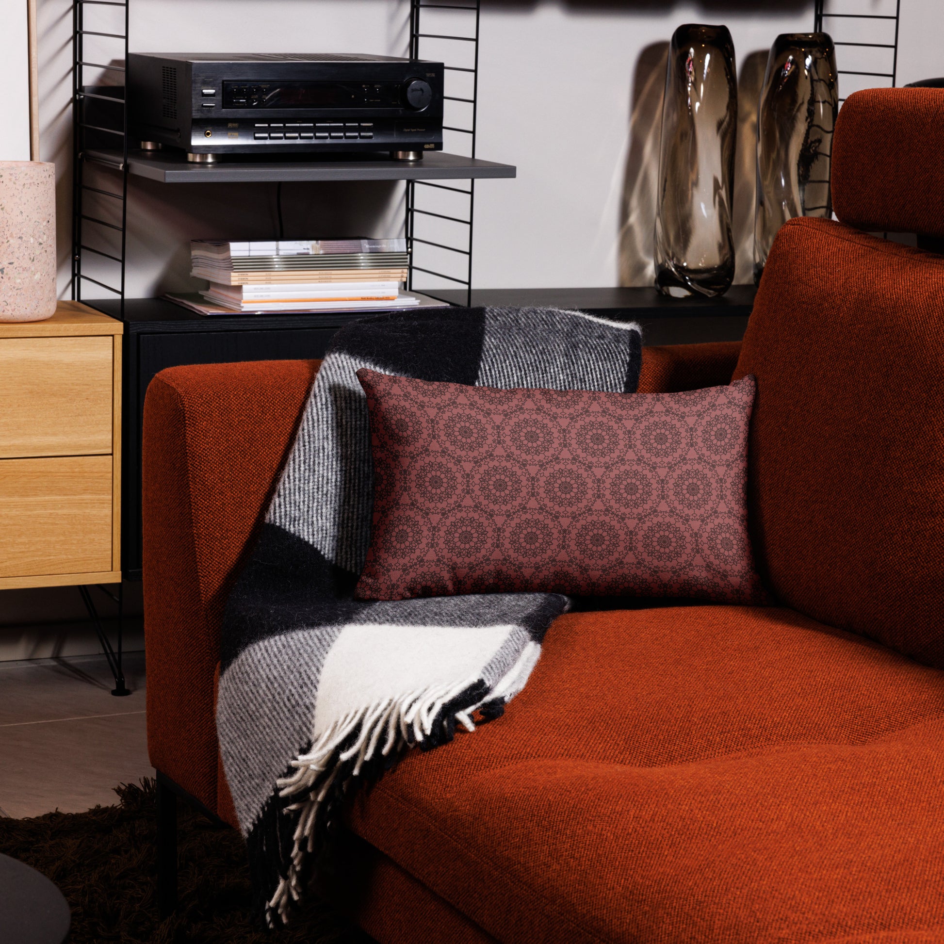 20″×12″ premium throw pillow with the 'Dodecagon' rose geometric pattern on orange armchair with checkered blanket.