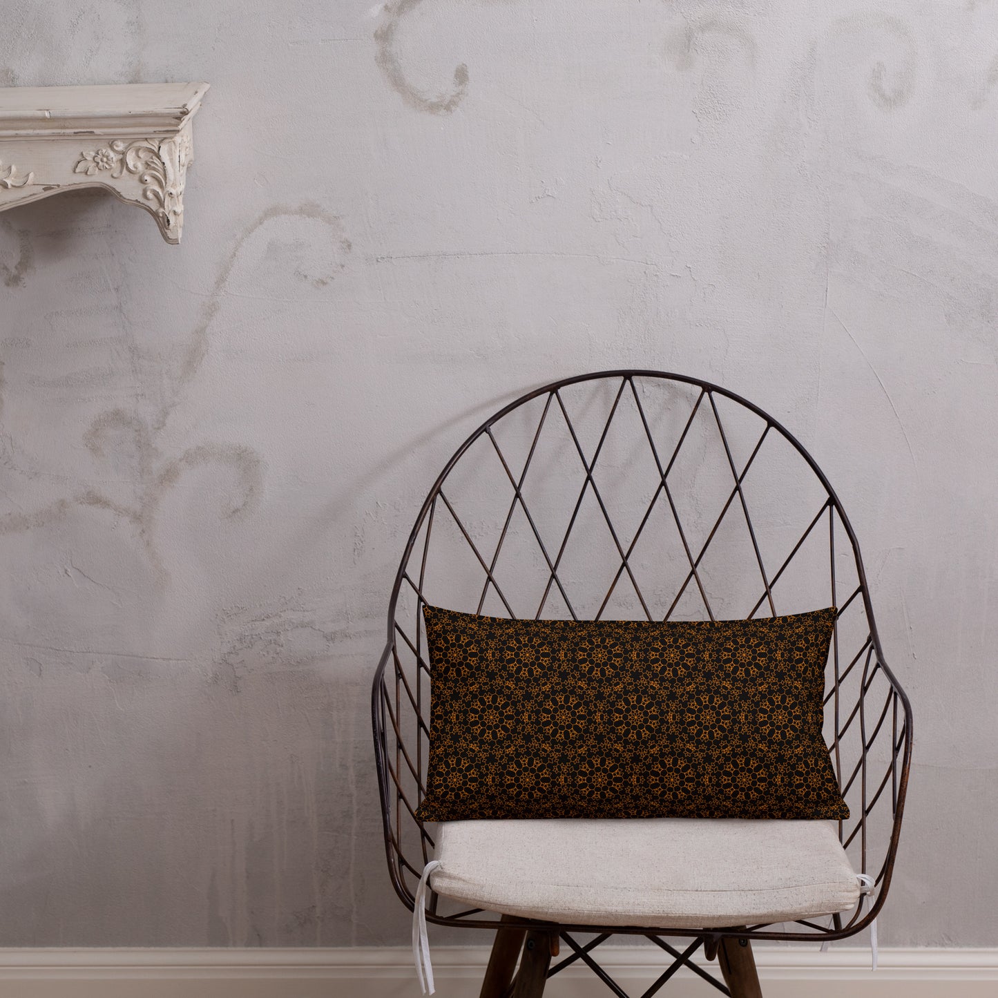 20″×12″ premium throw pillow with the 'Enneagon' black & gold geometric pattern on a wire chair.