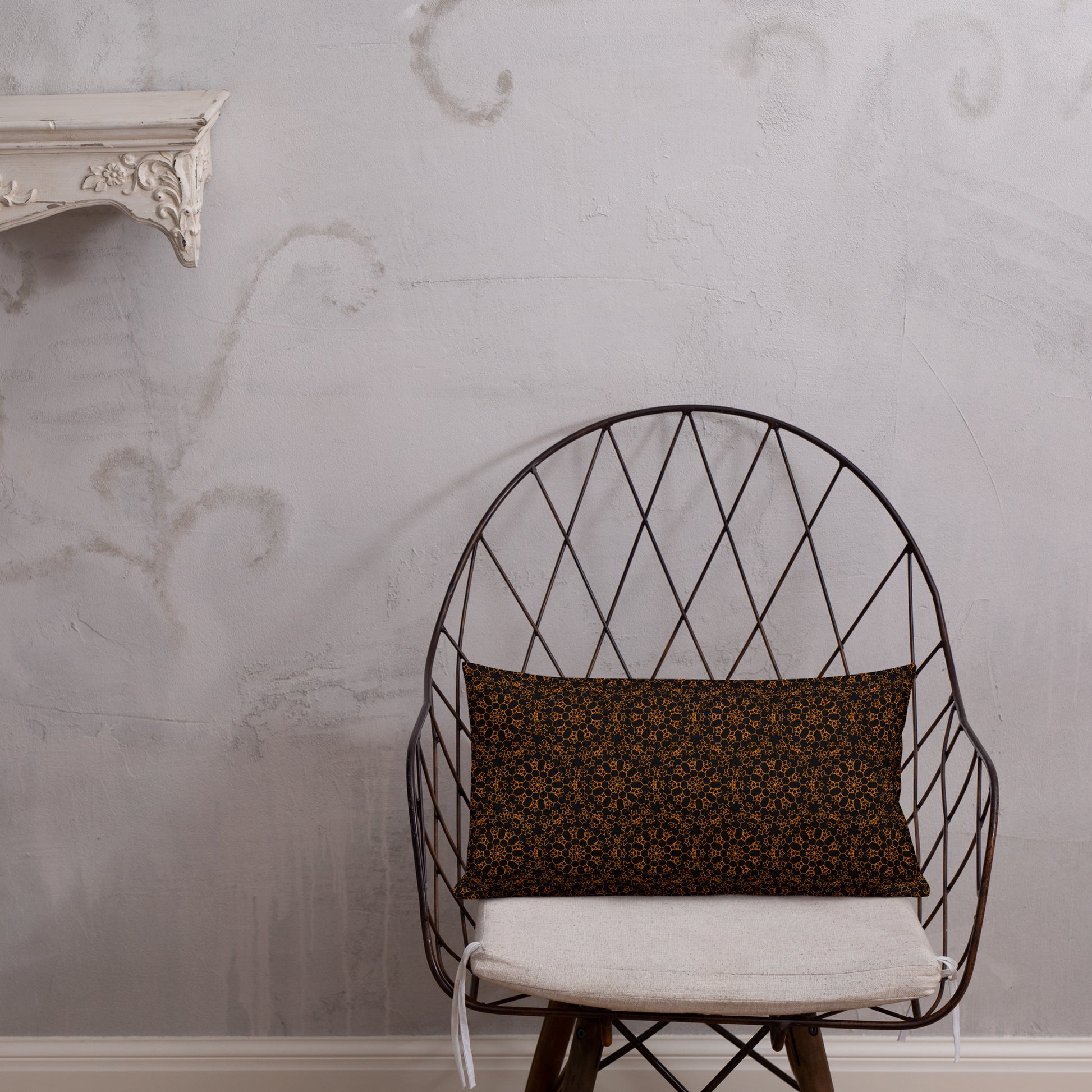 20″×12″ premium throw pillow with the 'Enneagon' black & gold geometric pattern on a wire chair.