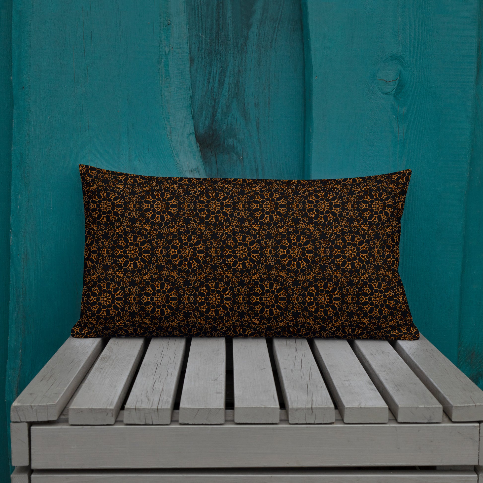 20″×12″ premium throw pillow with the 'Enneagon' black & gold geometric pattern on a wooden bench with teal wall.