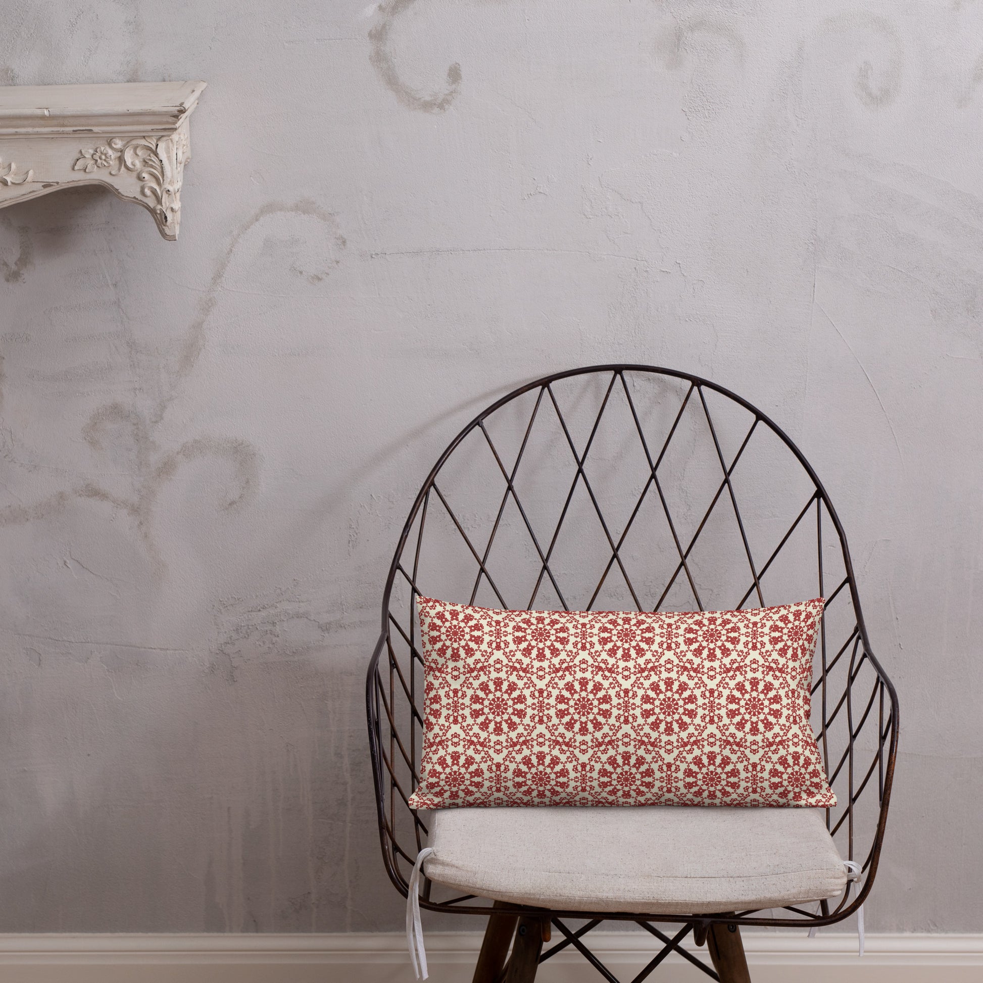 20″×12″ premium throw pillow with the ‘Decagon’ terracotta and beige geometric pattern on a wire chair against an ornate plaster wall.