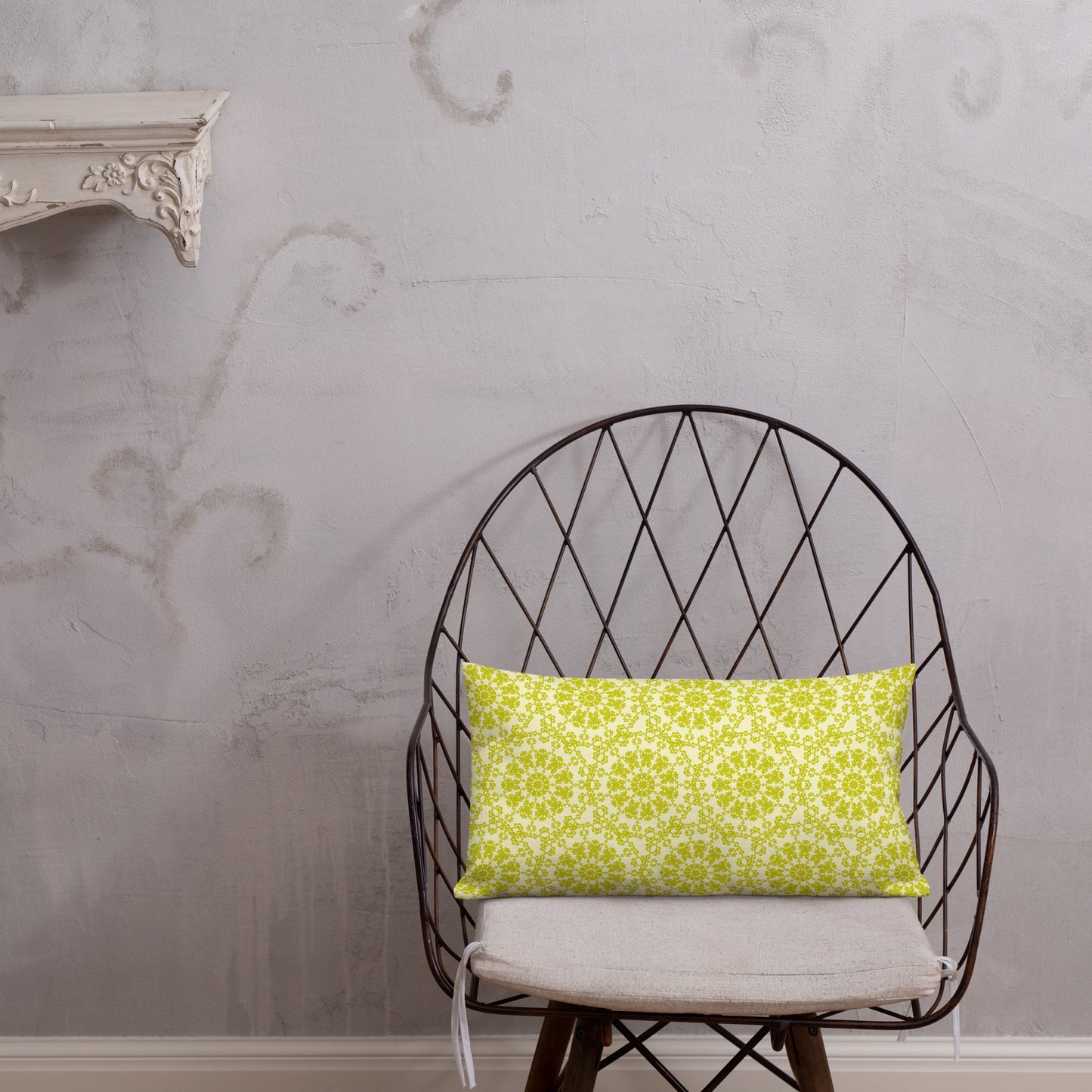 20″×12″ premium throw pillow with the 'Hendecagon' yellow-green geometric pattern on a wire chair with white plaster wall