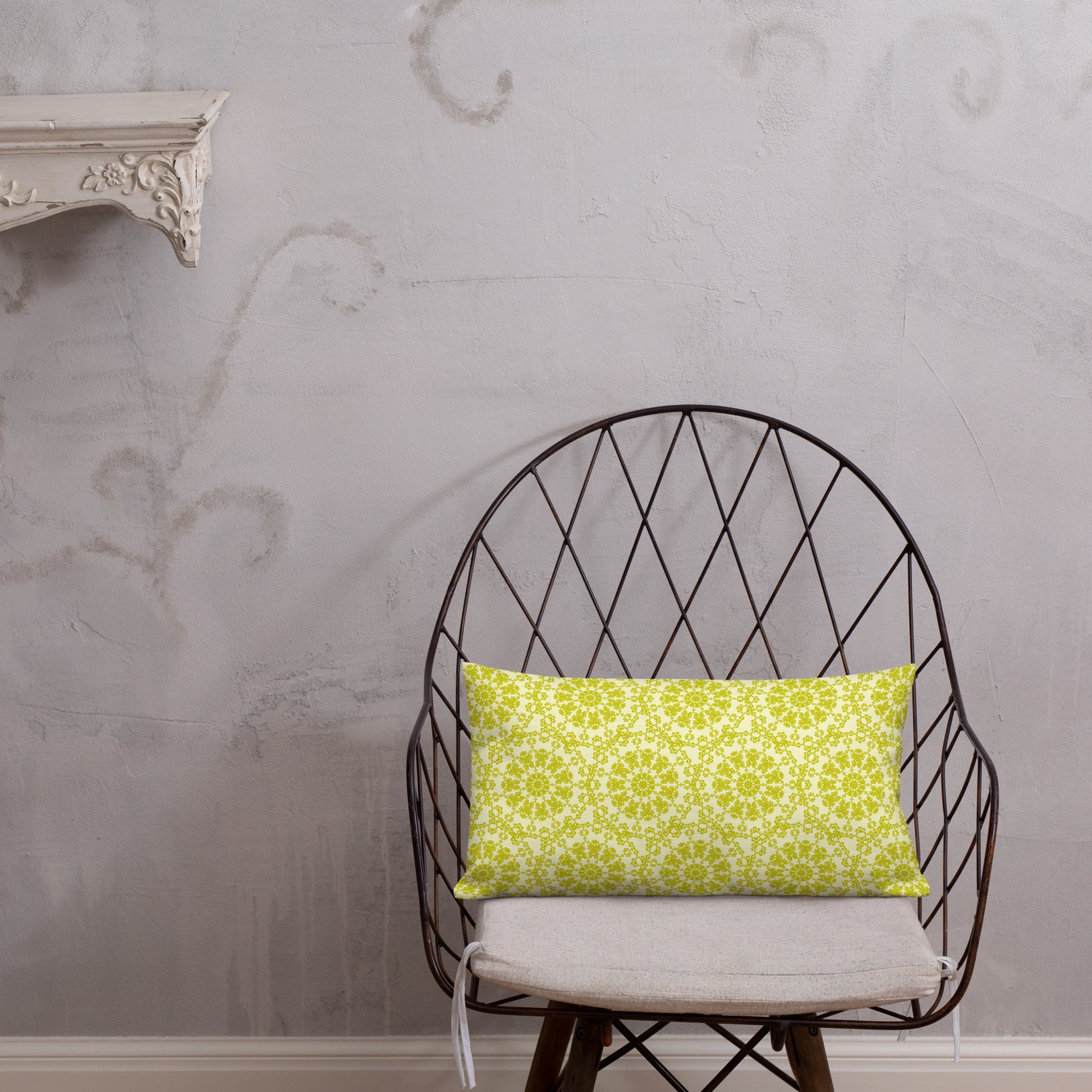 20″×12″ premium throw pillow with the 'Hendecagon' yellow-green geometric pattern on a wire chair with white plaster wall