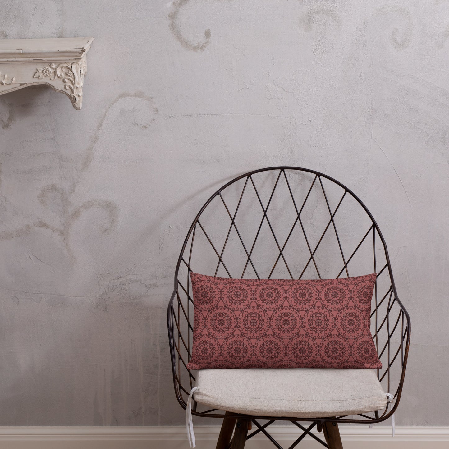 20″×12″ premium throw pillow with the 'Dodecagon' rose geometric pattern on wire chair with white cushion against textured wall.
