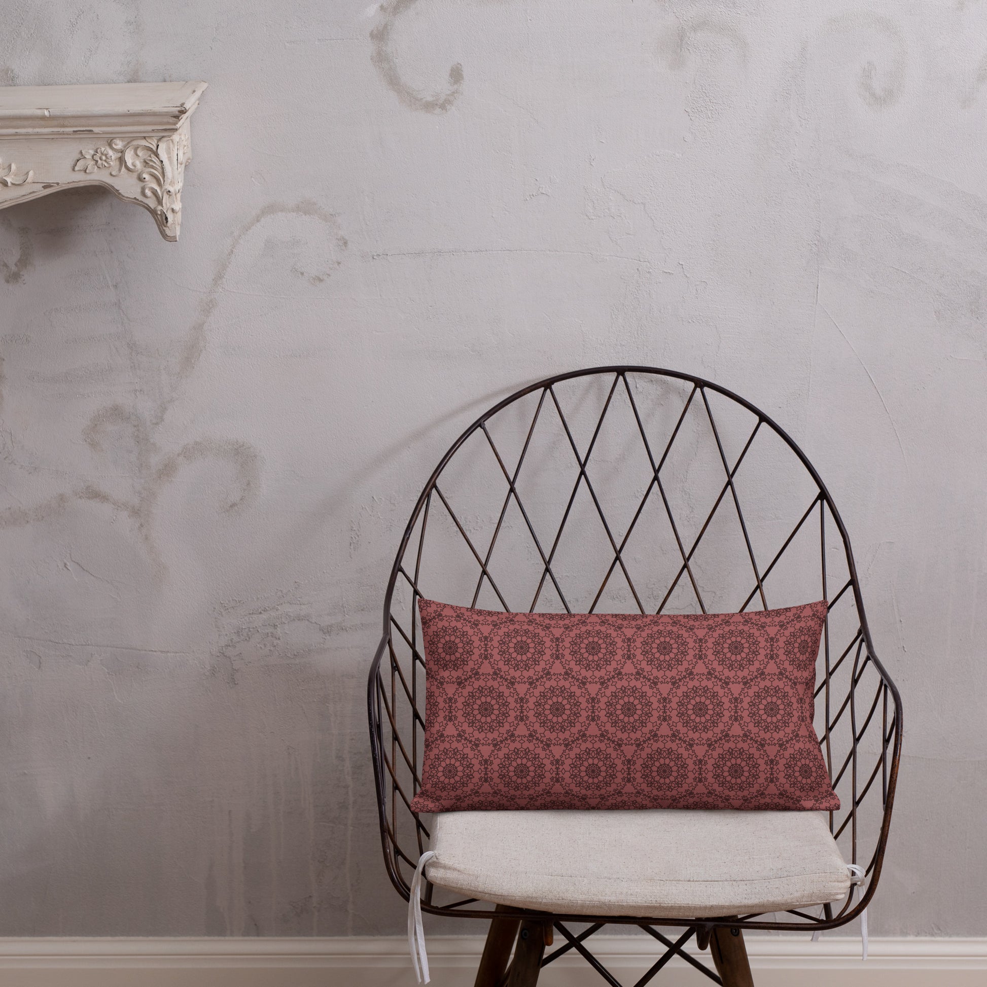 20″×12″ premium throw pillow with the 'Dodecagon' rose geometric pattern on wire chair with white cushion against textured wall.