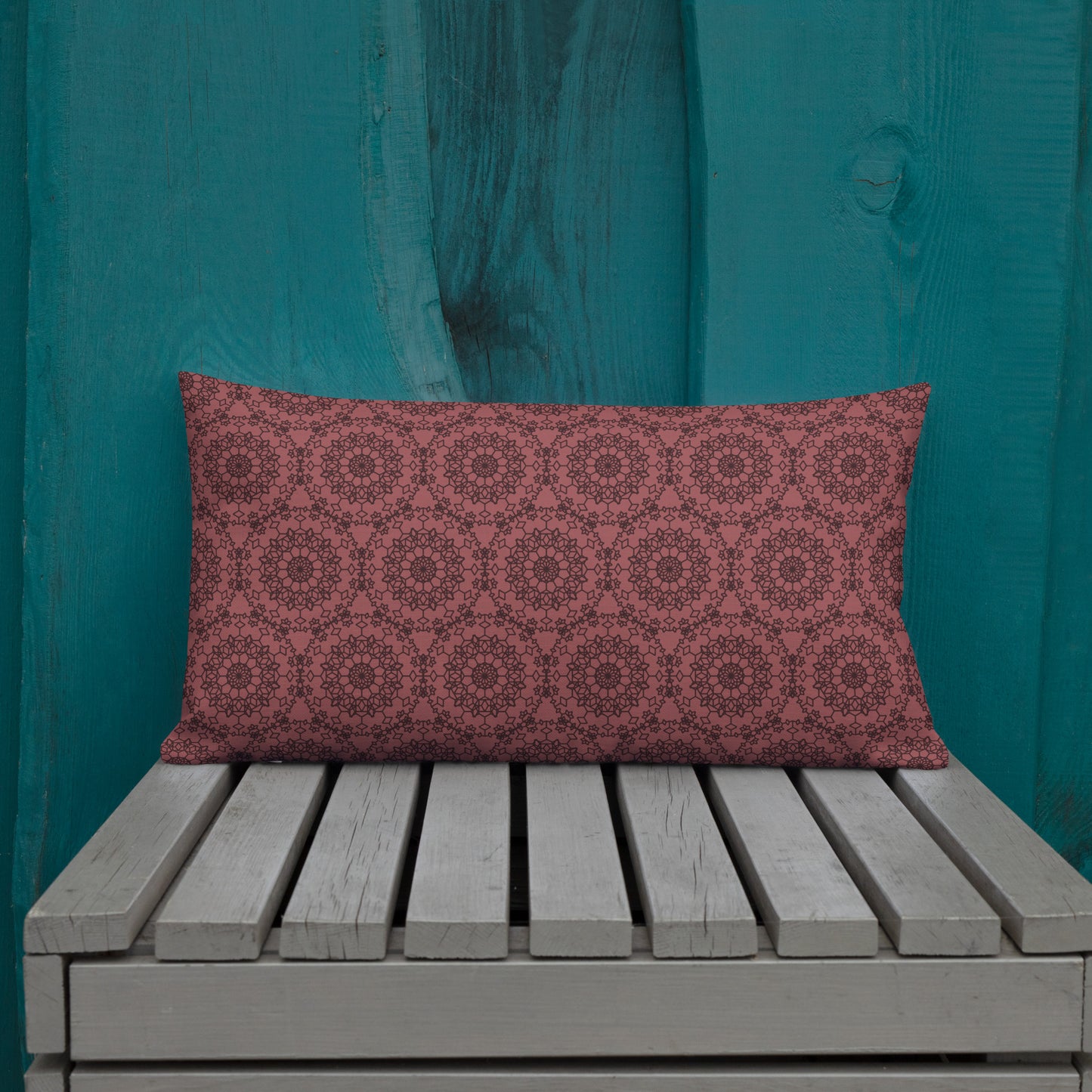 20″×12″ premium throw pillow with the 'Dodecagon' rose geometric pattern on wooden bench against teal painted wall.