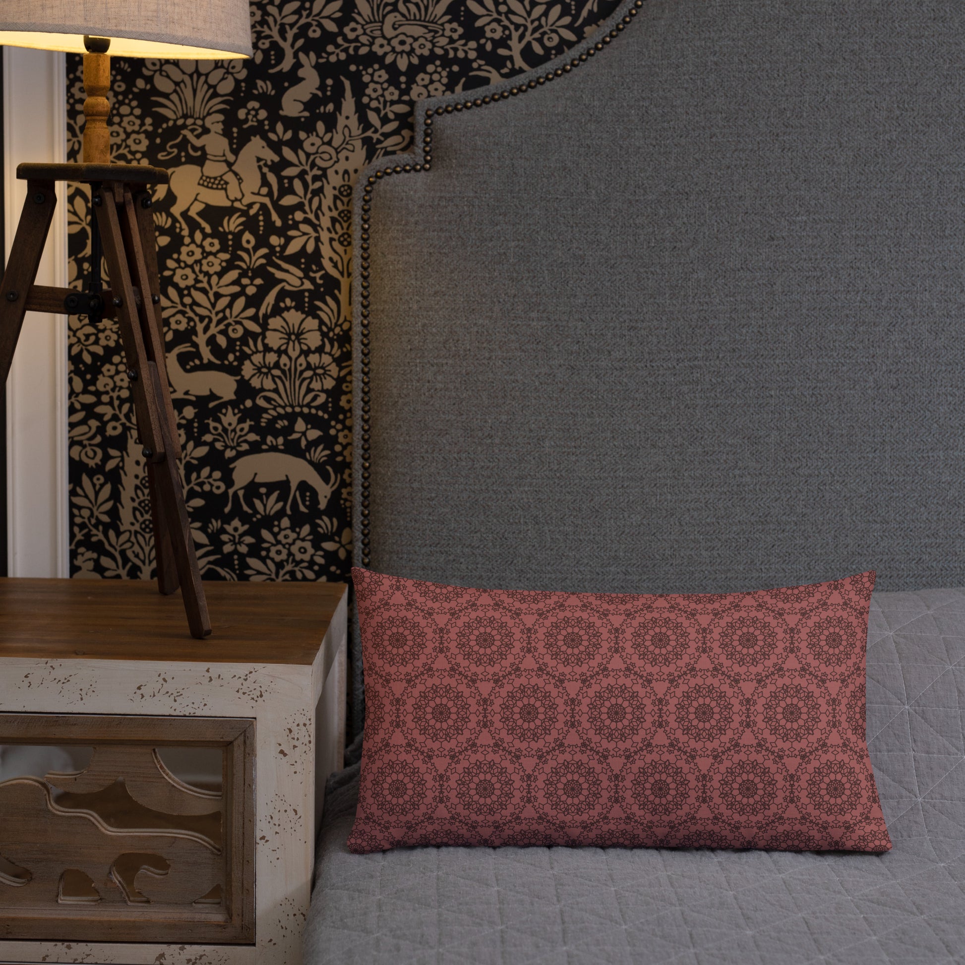 20″×12″ premium throw pillow with the 'Dodecagon' rose geometric pattern on bed beside grey upholstered headboard with lamp.