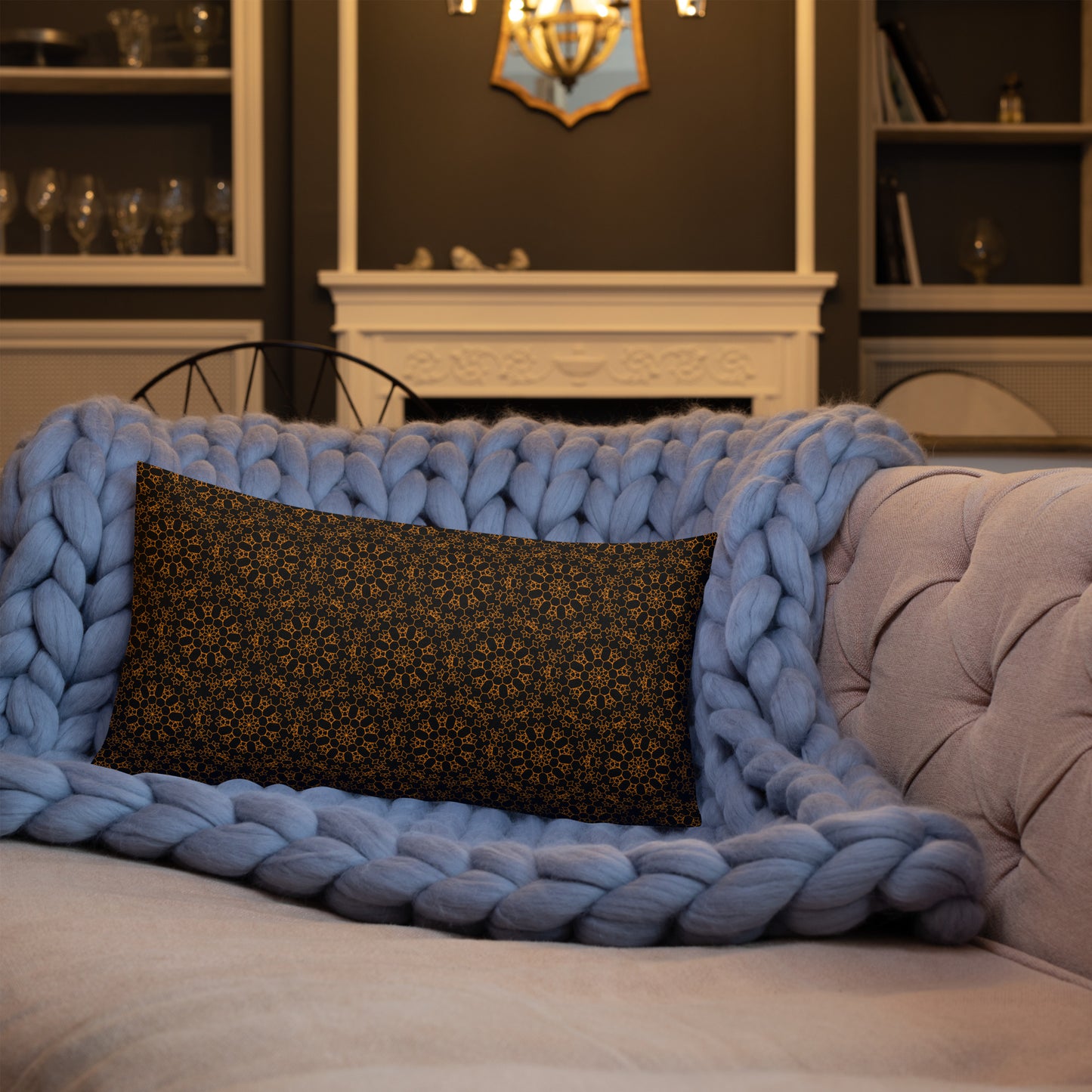 20″×12″ premium throw pillow with the 'Enneagon' black & gold geometric pattern on a sofa with chunky knit blanket.