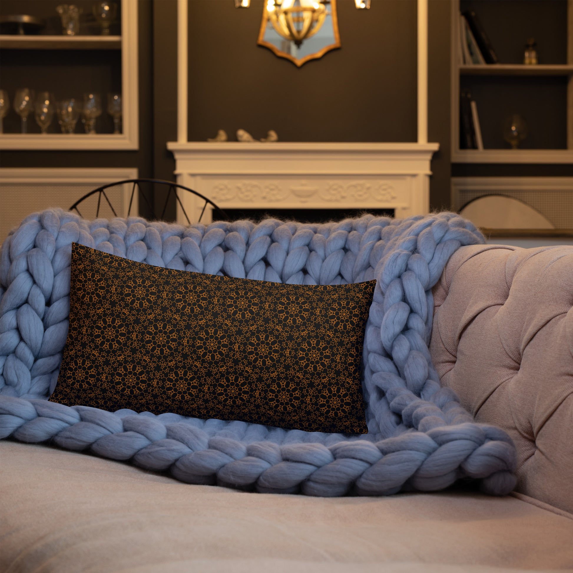 20″×12″ premium throw pillow with the 'Enneagon' black & gold geometric pattern on a sofa with chunky knit blanket.