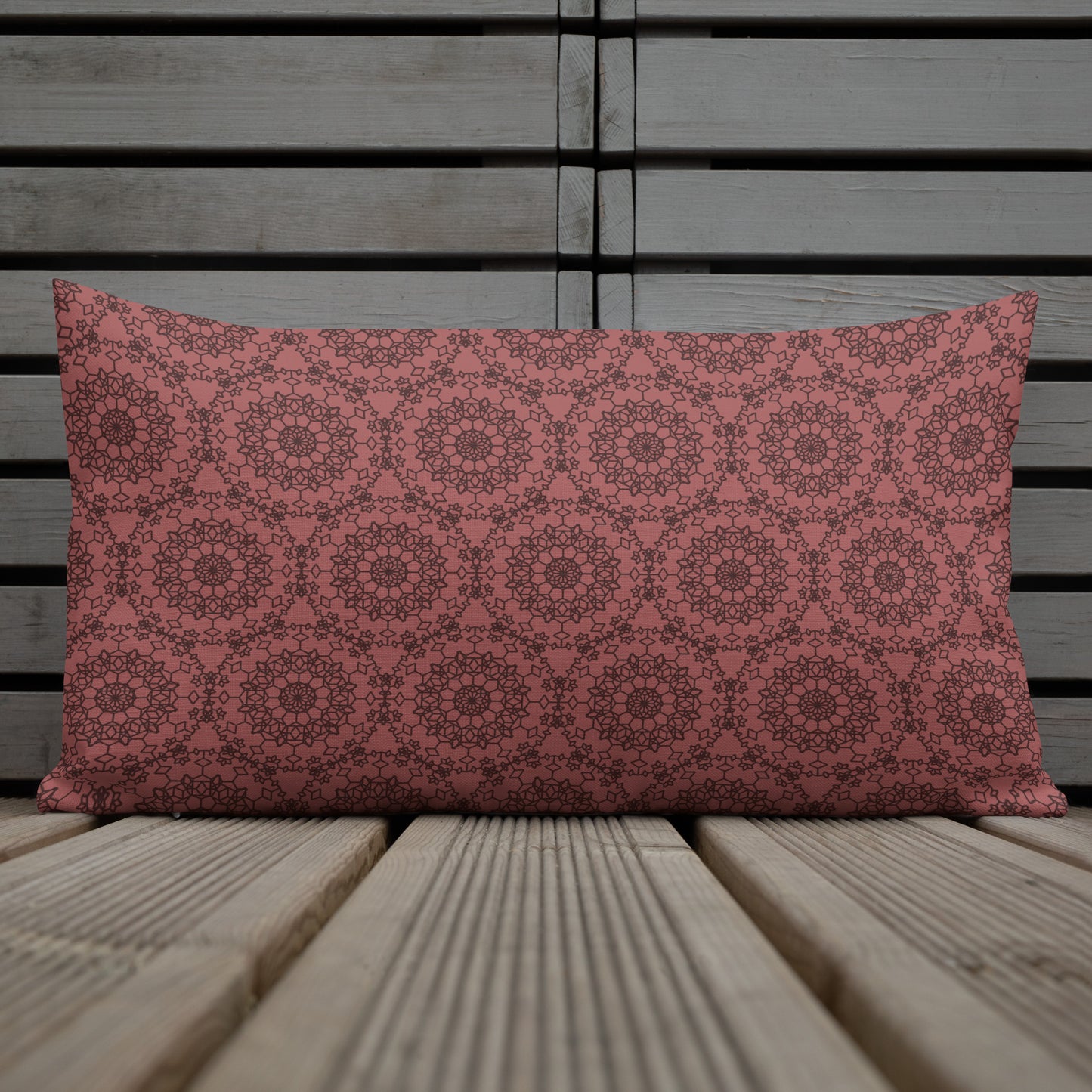 20″×12″ premium throw pillow with the 'Dodecagon' rose geometric pattern on wire chair beside side table with coffee cup.