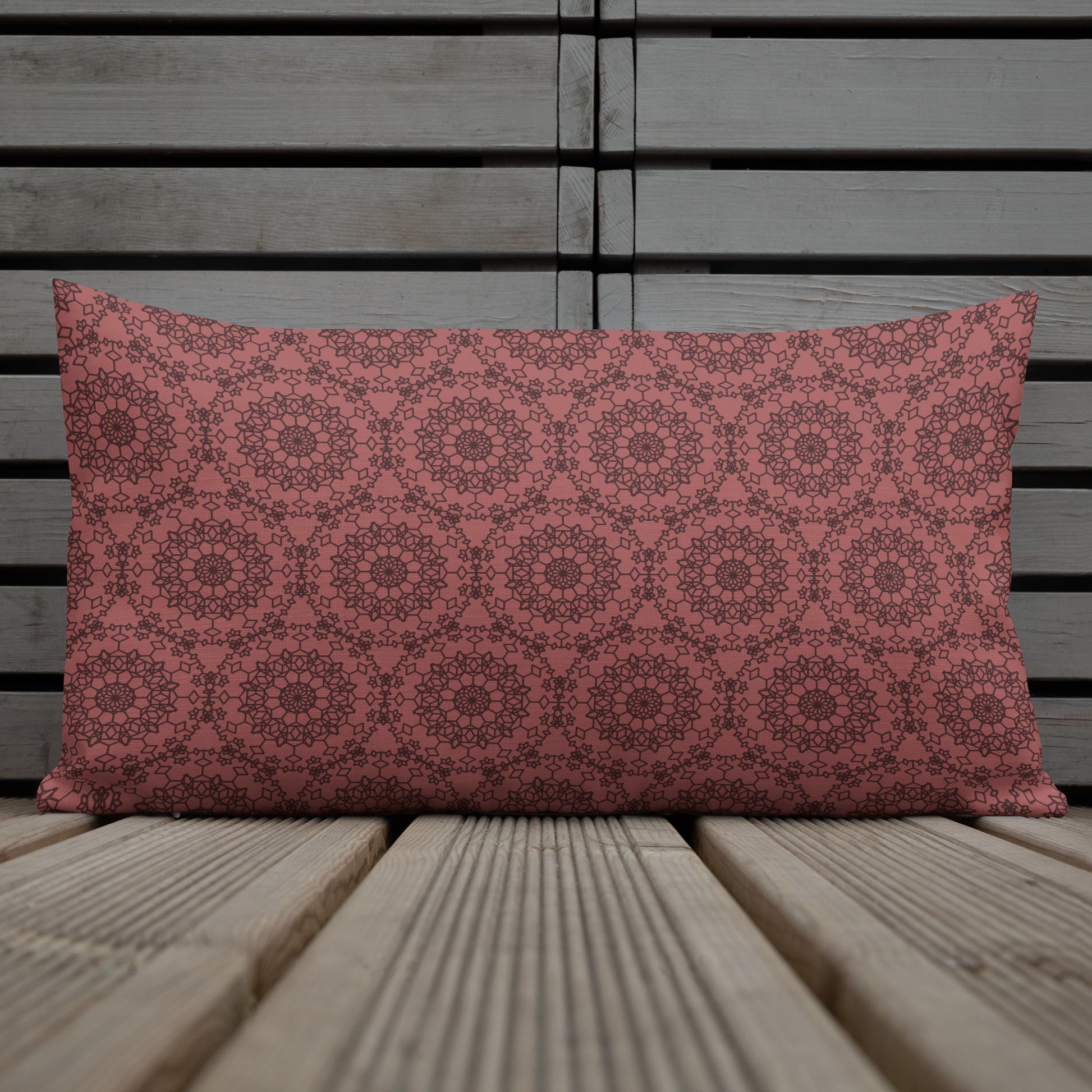 20″×12″ premium throw pillow with the 'Dodecagon' rose geometric pattern on wire chair beside side table with coffee cup.