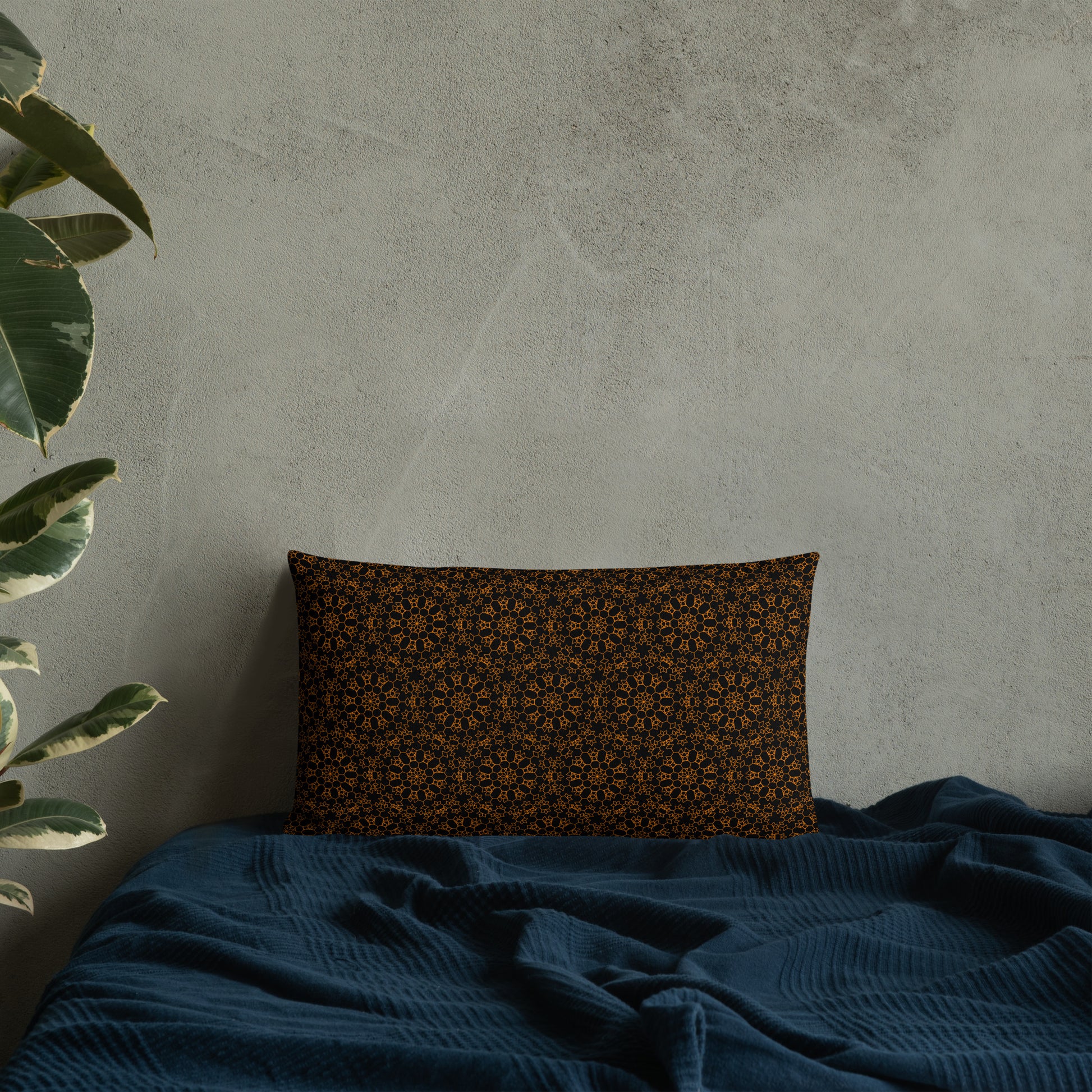 20″×12″ premium throw pillow with the 'Enneagon' black & gold geometric pattern on a bed with dark teal blanket.