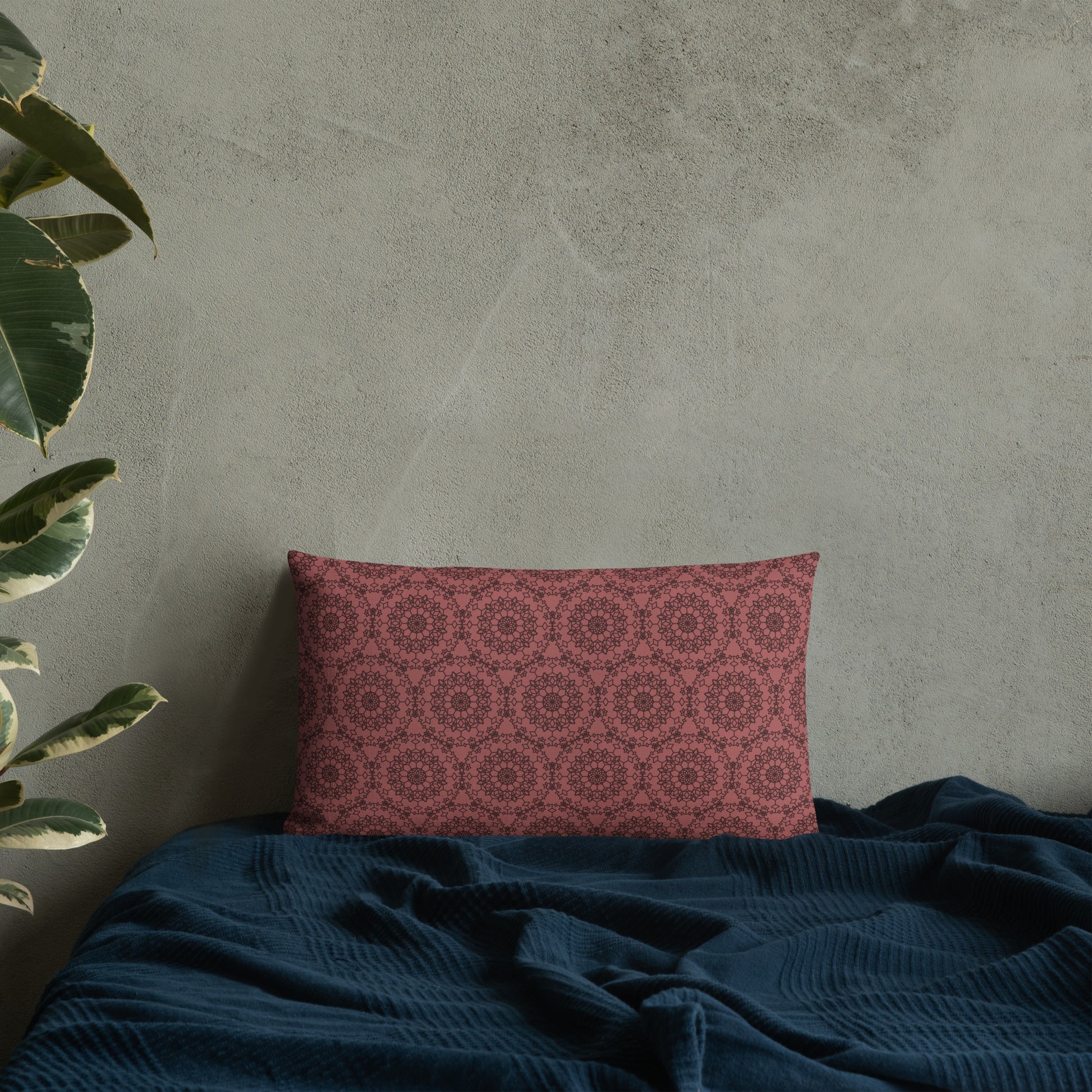 20″×12″ premium throw pillow with the 'Dodecagon' rose geometric pattern on bed with dark teal blanket against concrete wall.