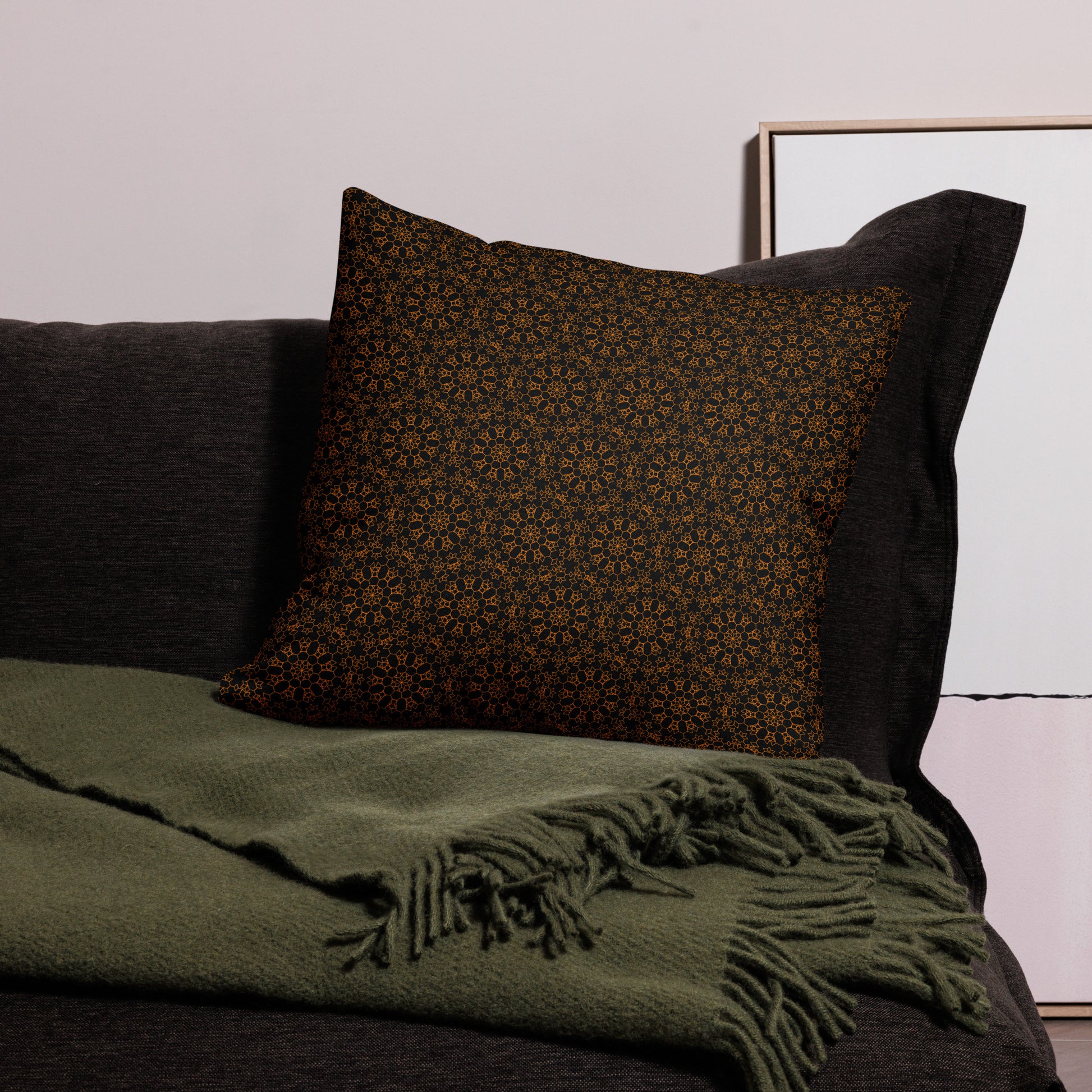 22″×22″ premium throw pillow with the 'Enneagon' black & gold geometric pattern on a dark sofa with green throw blanket.
