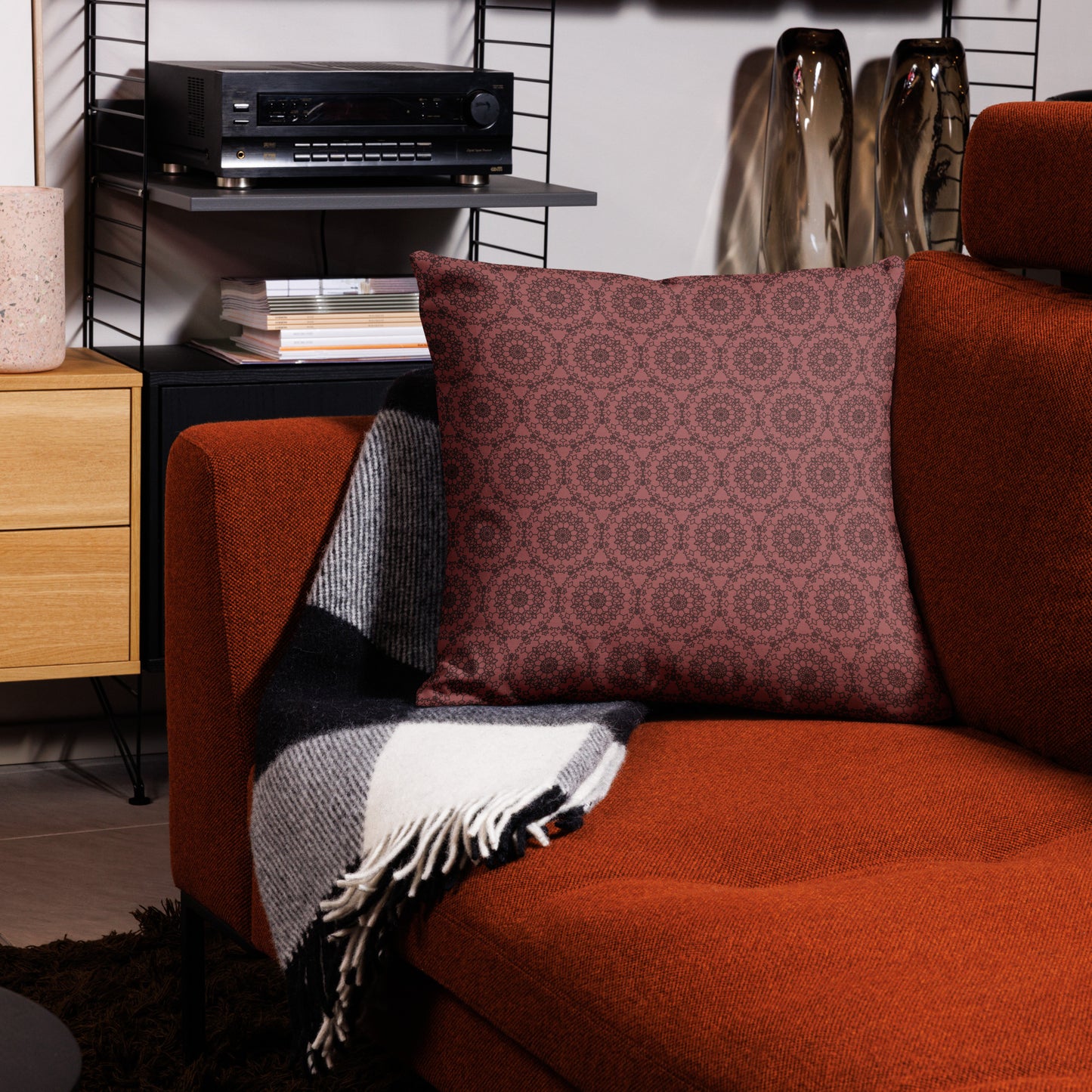 22″×22″ premium throw pillow with the 'Dodecagon' rose geometric pattern on orange armchair with checkered blanket.
