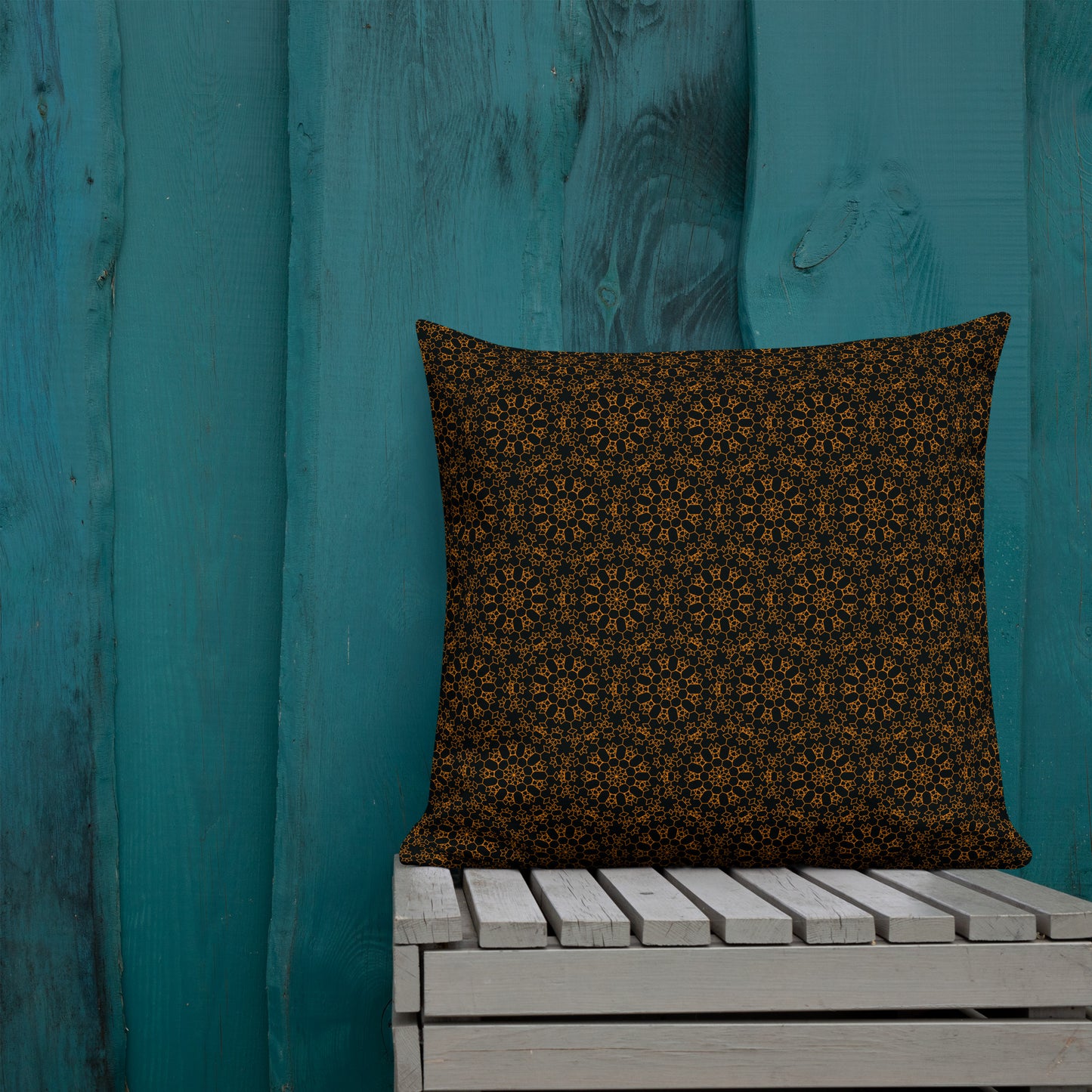 22″×22″ premium throw pillow with the 'Enneagon' black & gold geometric pattern on a wooden bench with teal wall.