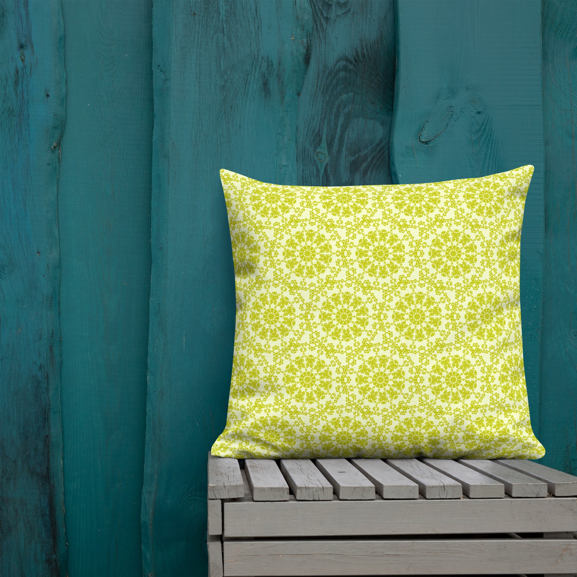 22″×22″ premium throw pillow with the 'Hendecagon' yellow-green geometric pattern on a wooden bench with teal wall