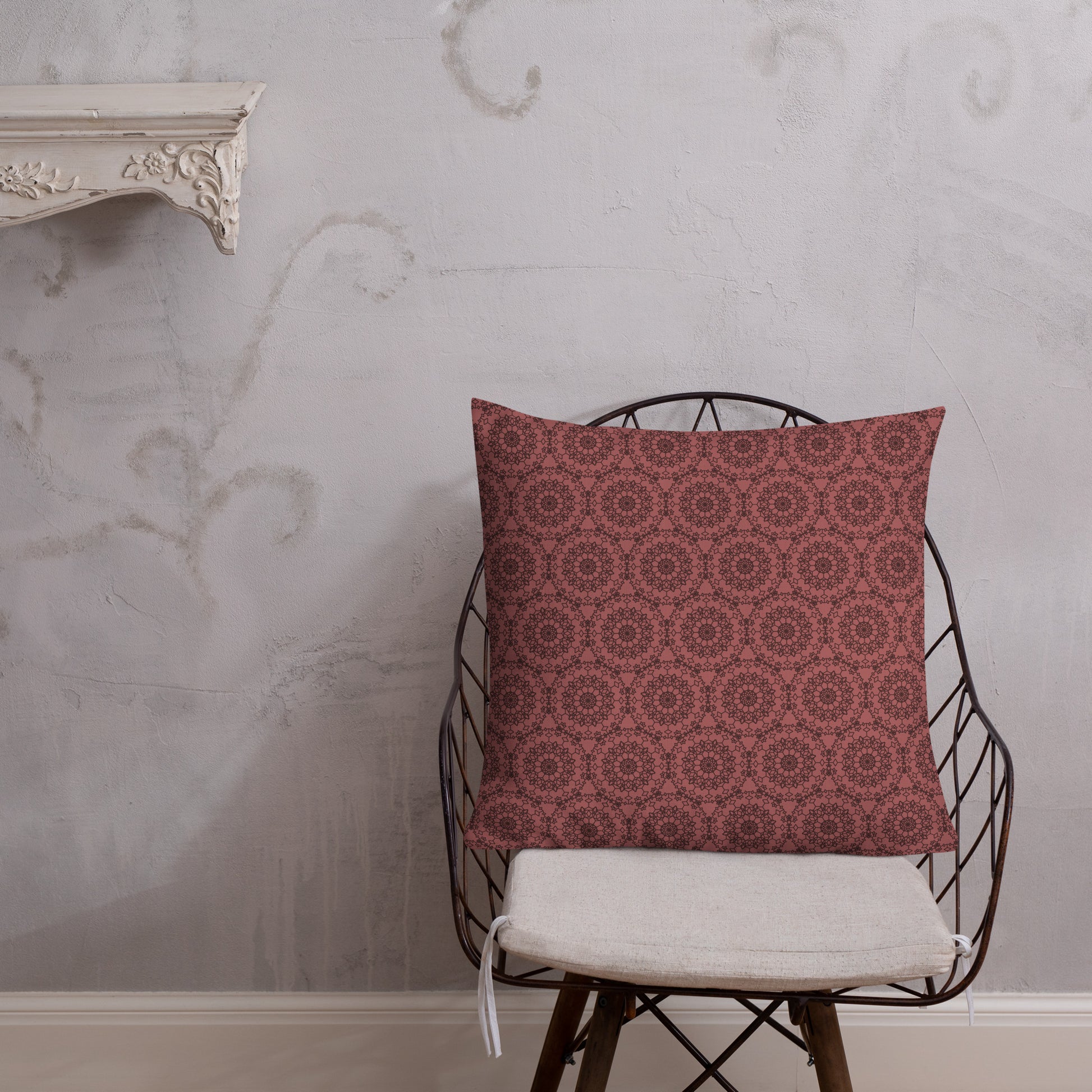 22″×22″ premium throw pillow with the 'Dodecagon' rose geometric pattern on wire chair with white cushion against textured wall.