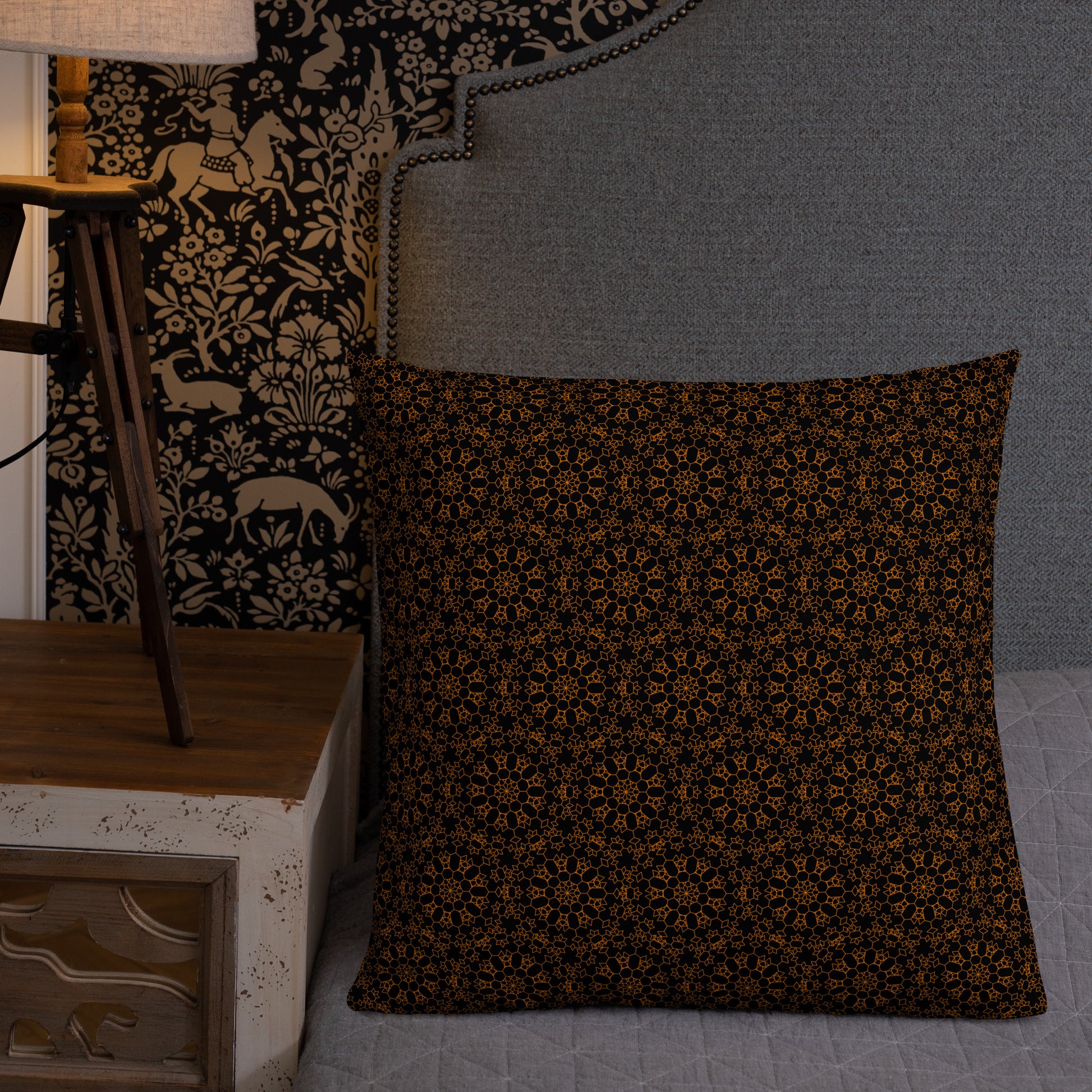 22″×22″ premium throw pillow with the 'Enneagon' black & gold geometric pattern on a bed with upholstered headboard.