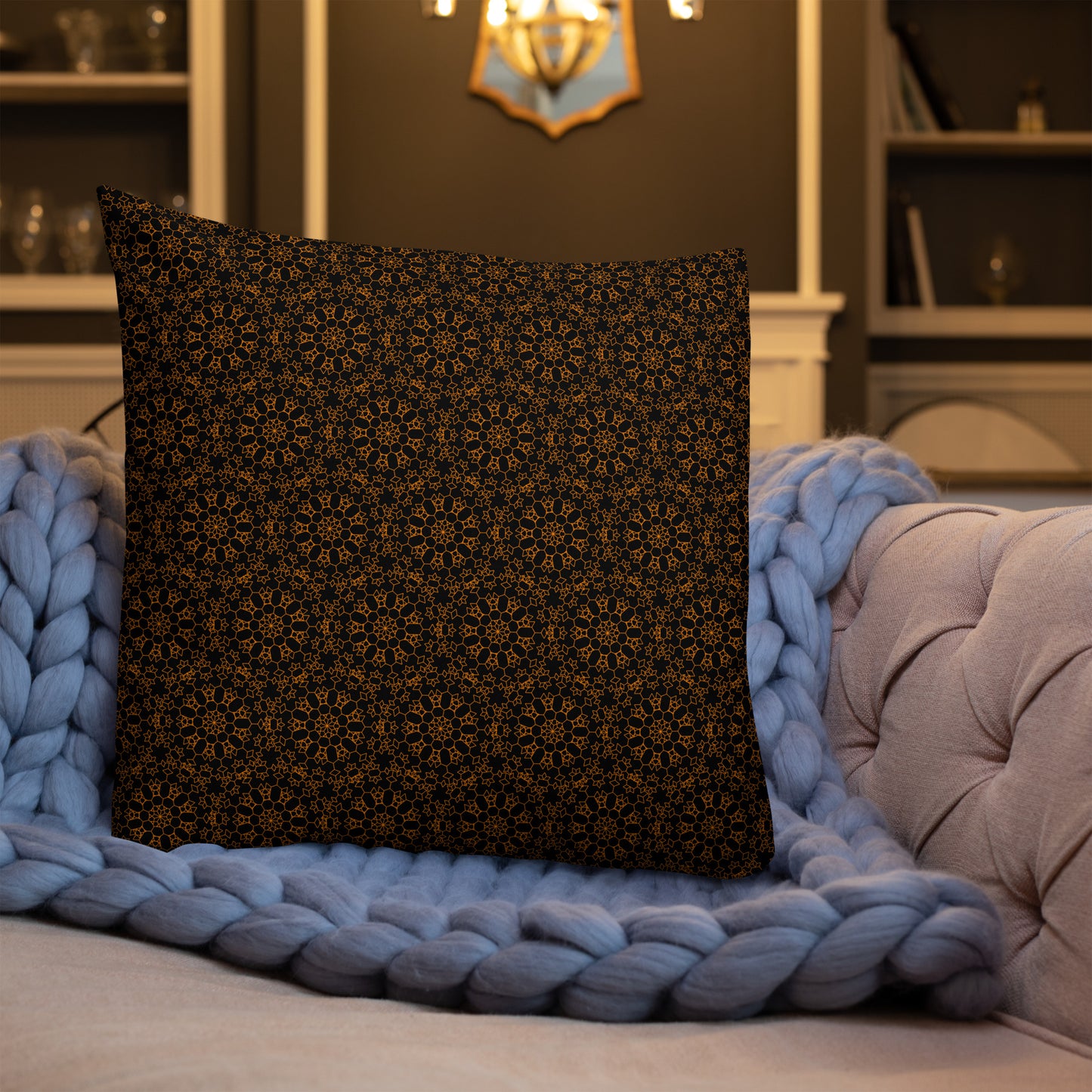 22″×22″ premium throw pillow with the 'Enneagon' black & gold geometric pattern on a sofa with chunky knit blanket.
