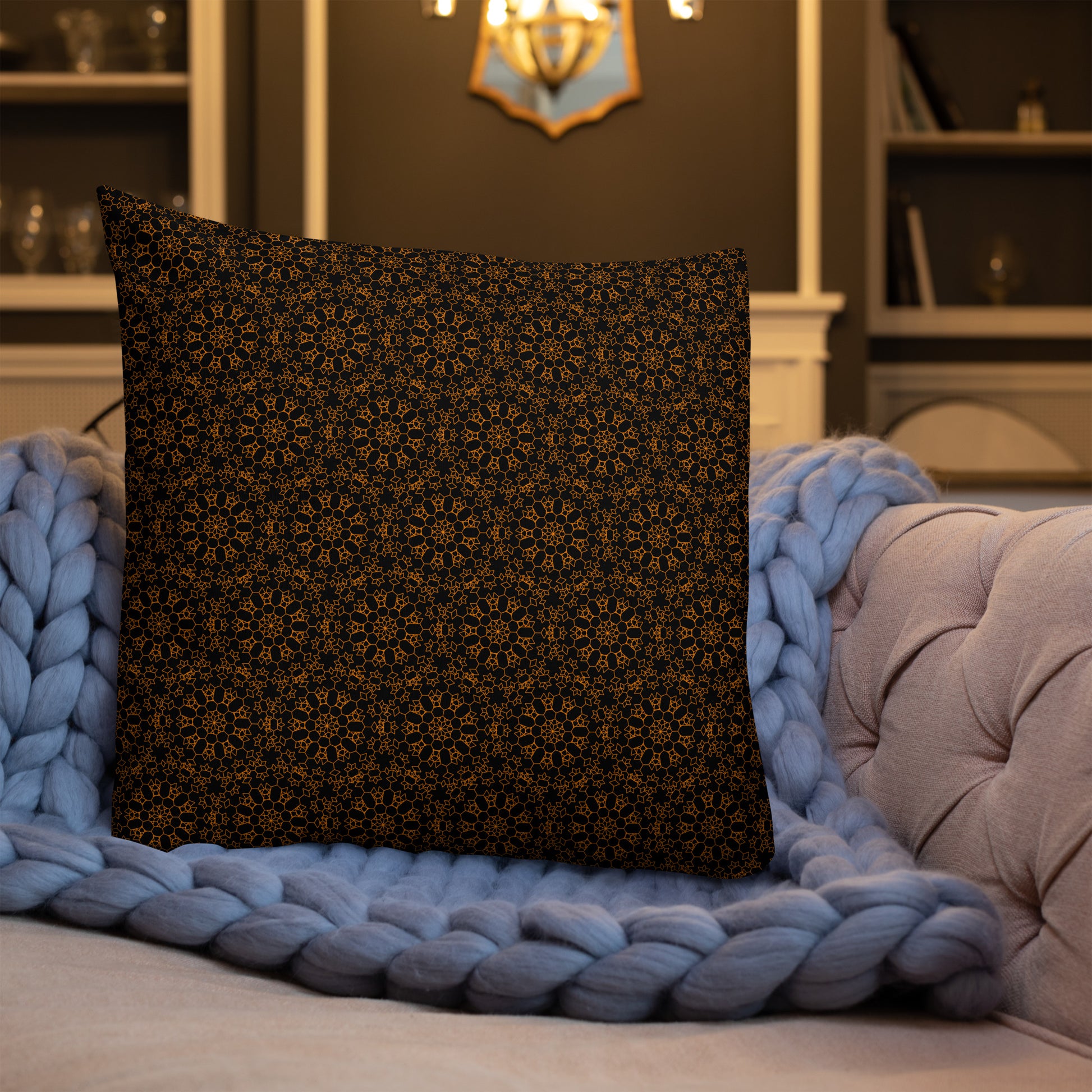 22″×22″ premium throw pillow with the 'Enneagon' black & gold geometric pattern on a sofa with chunky knit blanket.