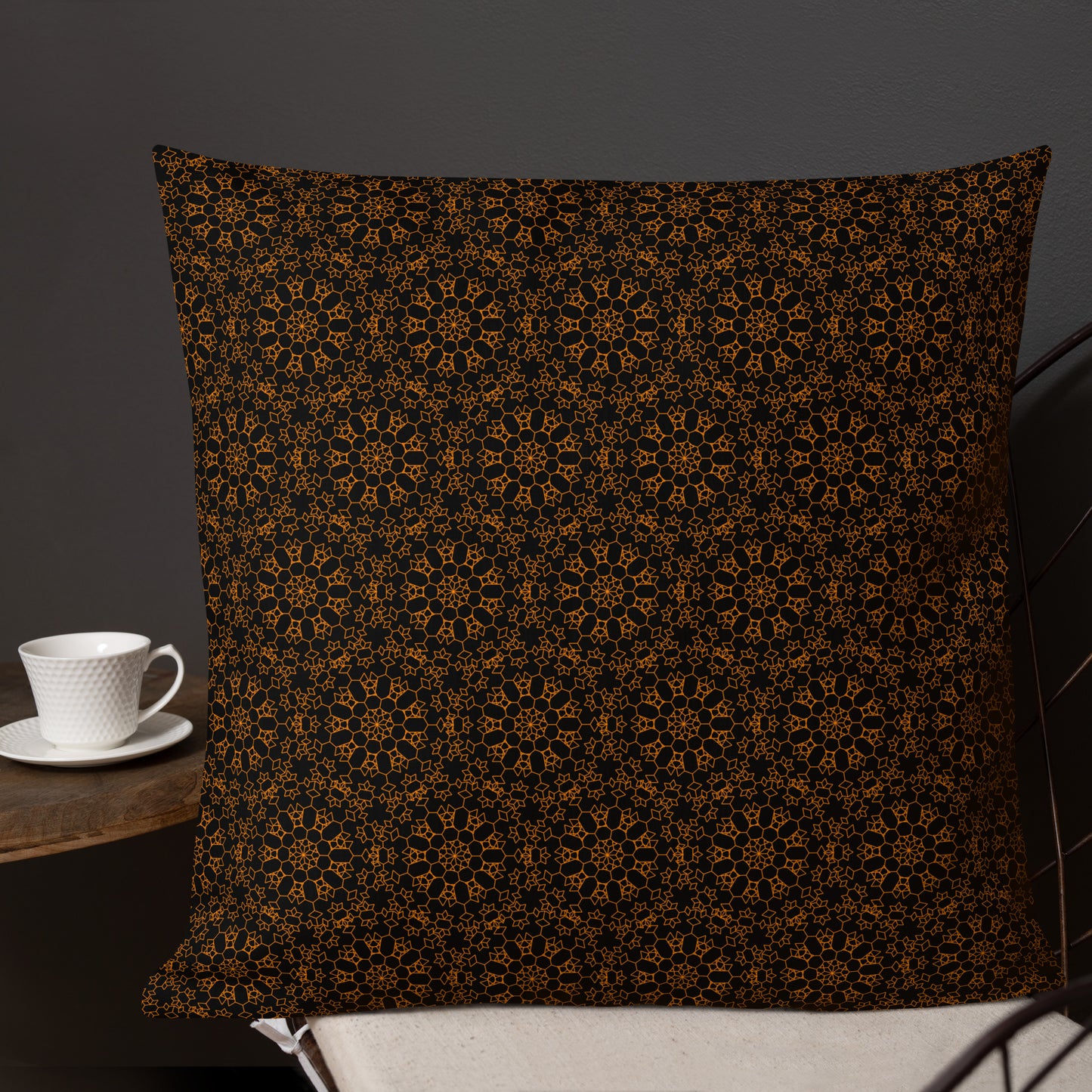 22″×22″ premium throw pillow with the 'Enneagon' black & gold geometric pattern on a chair with coffee cup on side table.