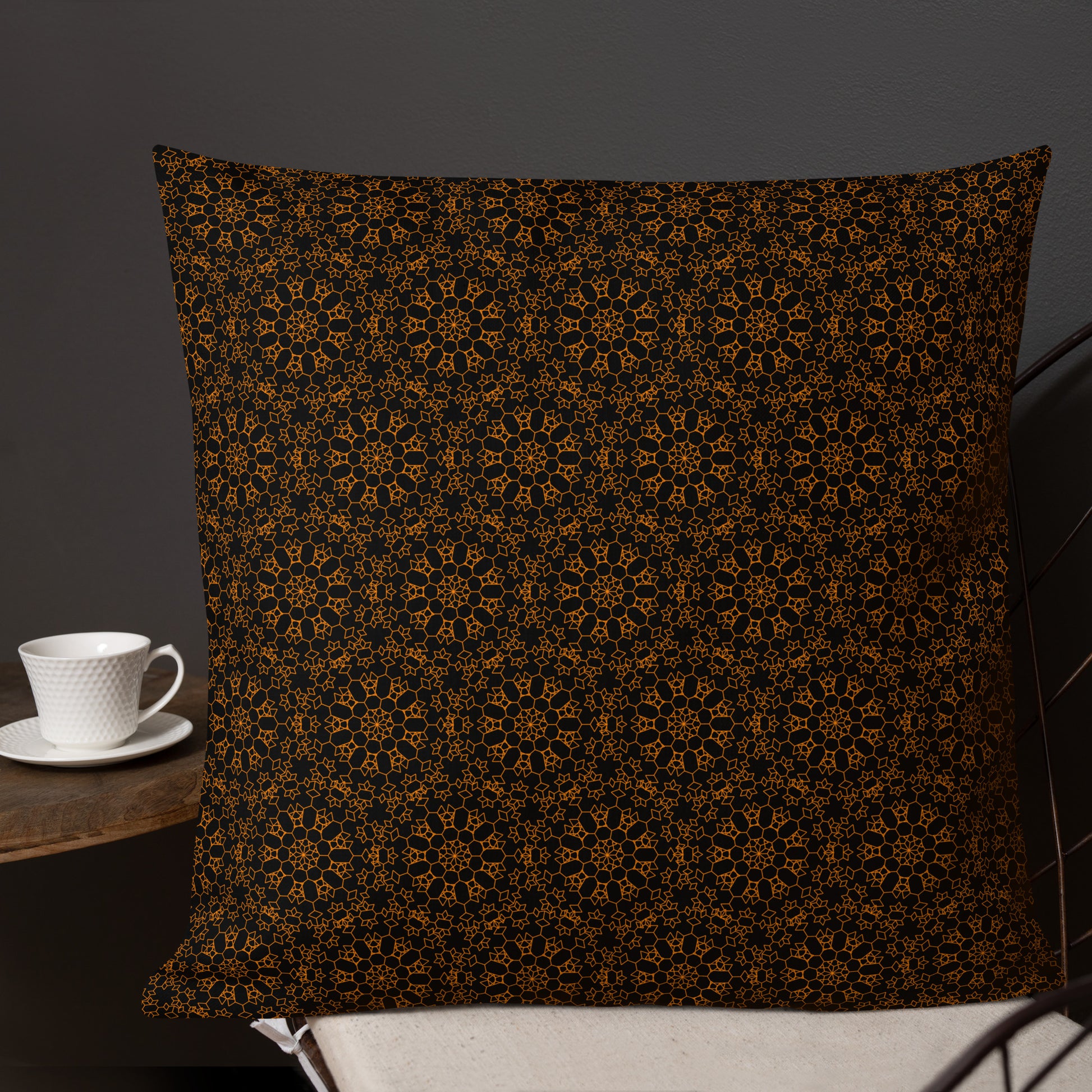 22″×22″ premium throw pillow with the 'Enneagon' black & gold geometric pattern on a chair with coffee cup on side table.