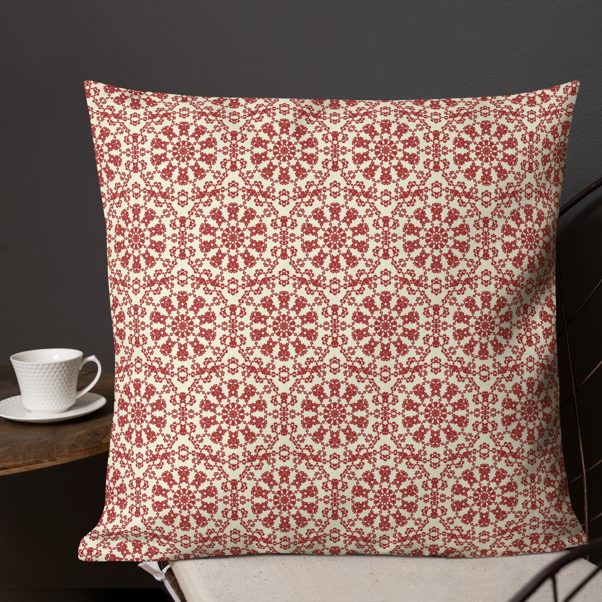 22″×22″ premium throw pillow with the ‘Decagon’ terracotta and beige geometric pattern on a dark chair with a coffee cup on a side table.