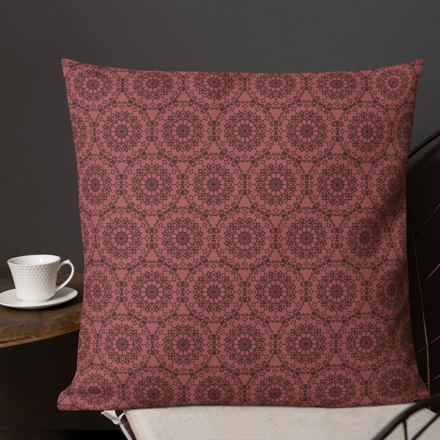 22″×22″ premium throw pillow with the 'Dodecagon' rose geometric pattern on wire chair beside side table with coffee cup.