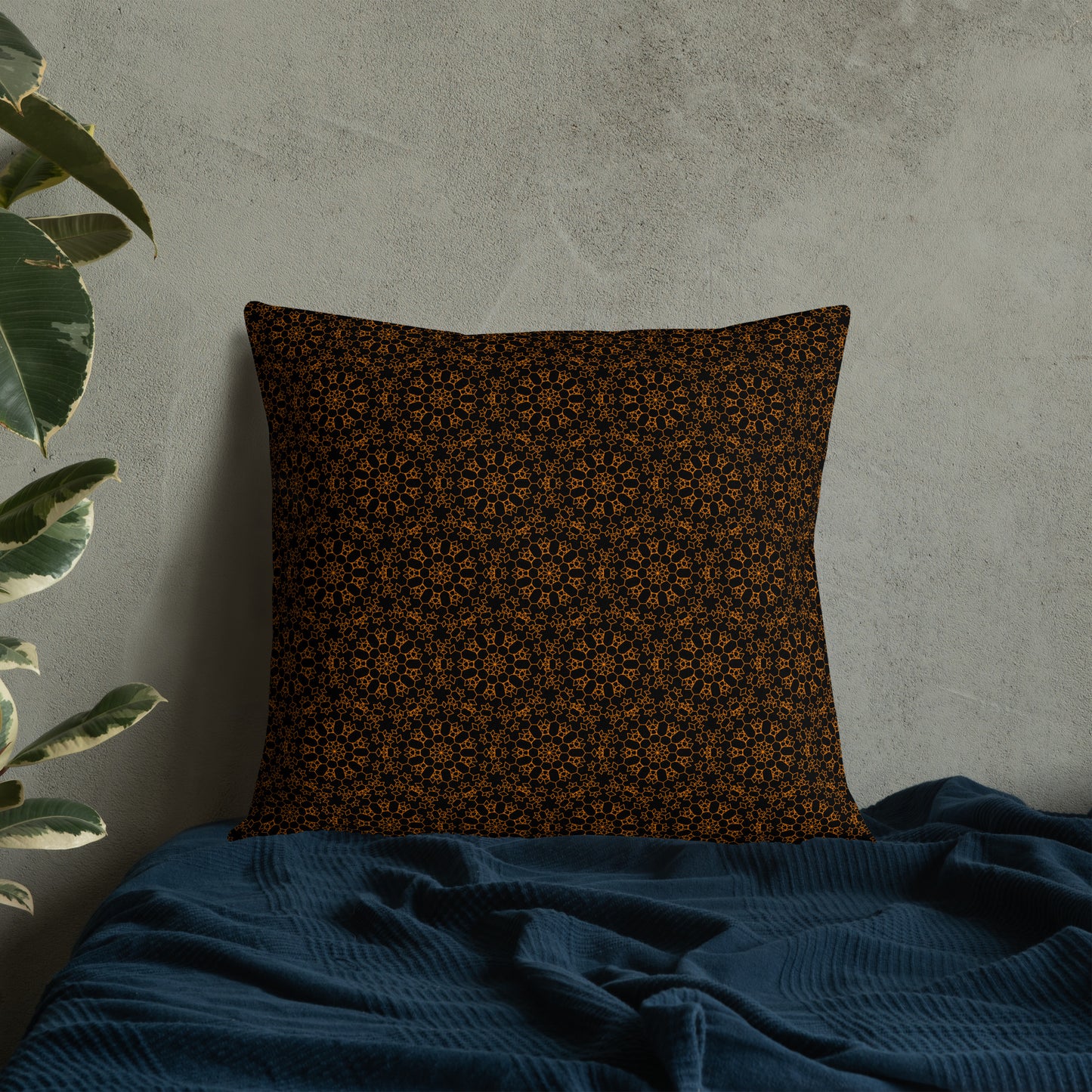 22″×22″ premium throw pillow with the 'Enneagon' black & gold geometric pattern on a bed with dark teal blanket.