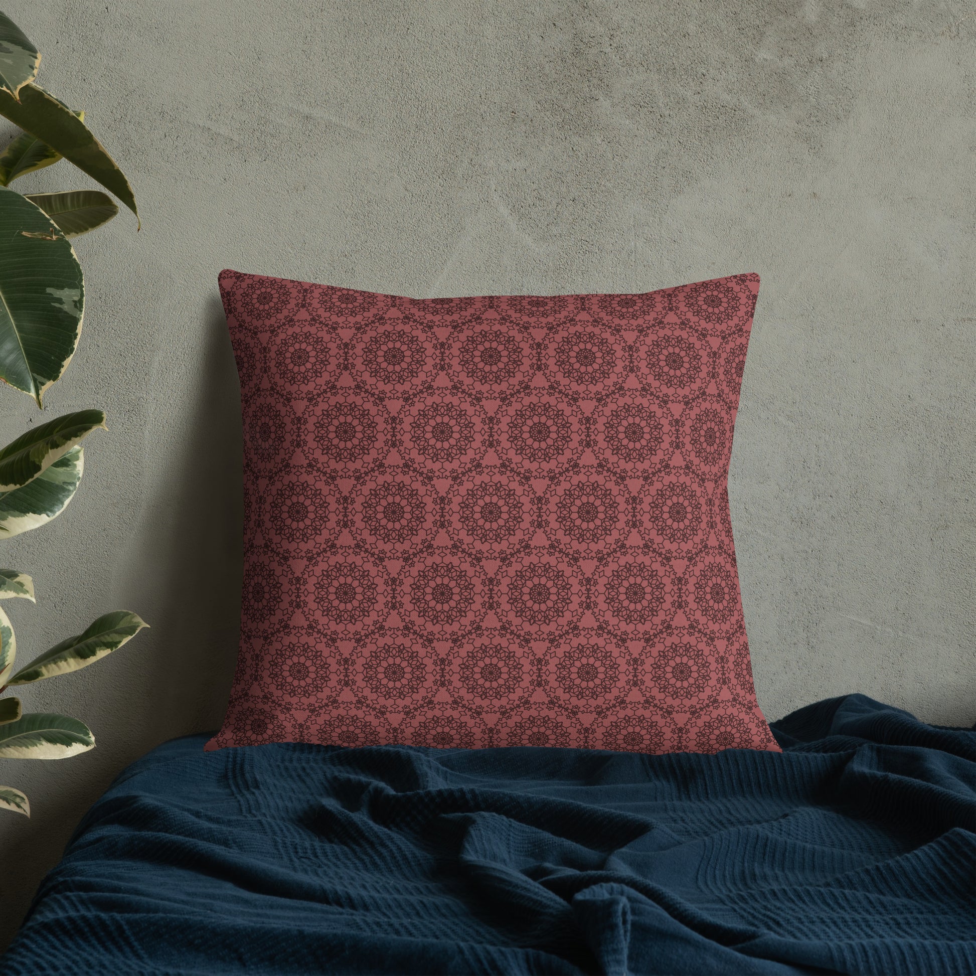 22″×22″ premium throw pillow with the 'Dodecagon' rose geometric pattern on bed with dark teal blanket against concrete wall.