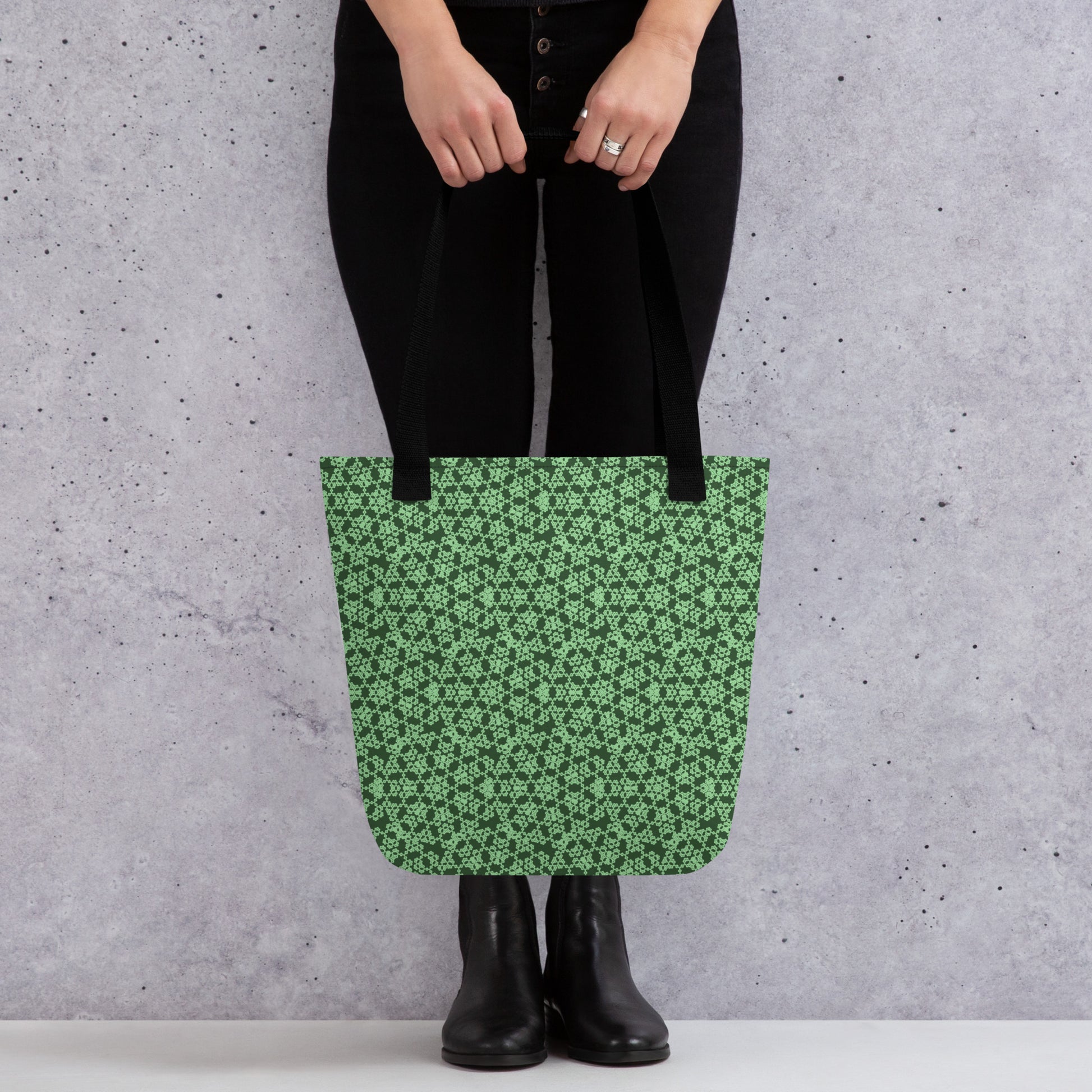 Close up of the lower part of a model holding with two hands the tote bag with the 'Heptagon' green fractal geometric pattern.