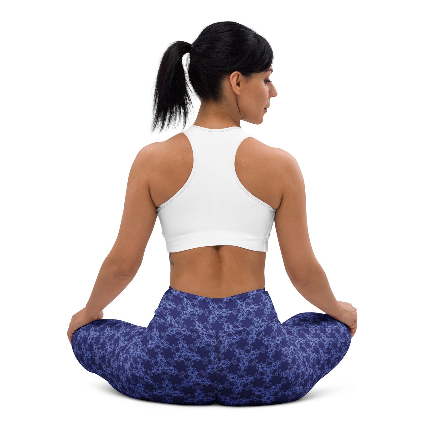 Back shot of a young woman sitting in lotus position wearing leggings with the 'Triagon' navy and blue fractal geometric pattern.