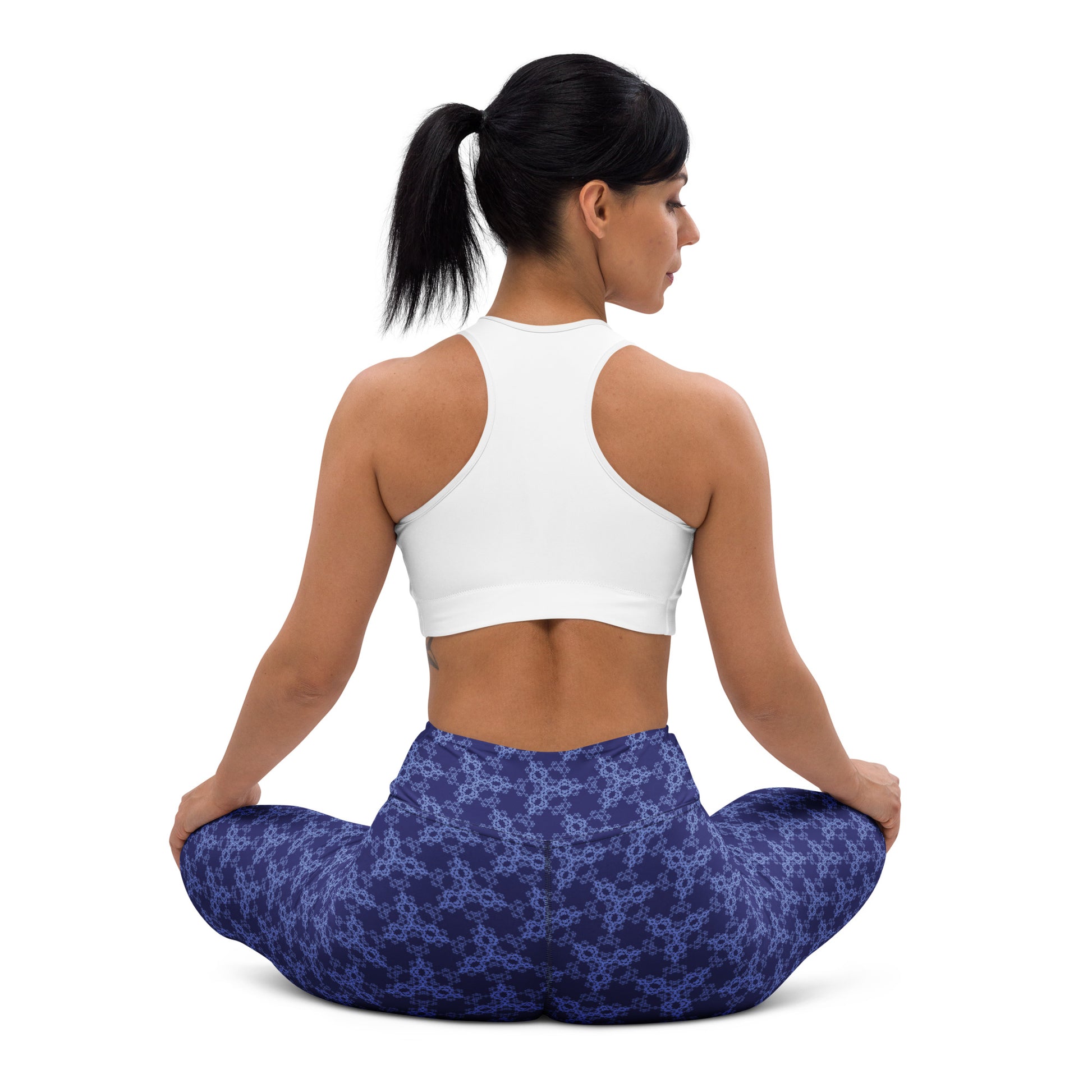 Back shot of a young woman sitting in lotus position wearing leggings with the 'Triagon' navy and blue fractal geometric pattern.