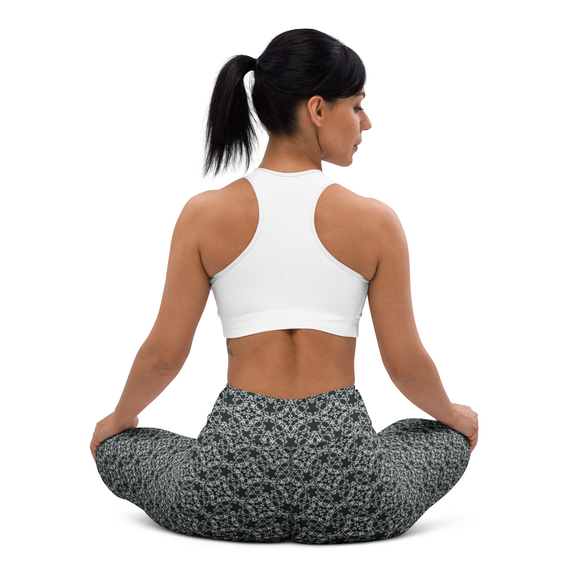 Back shot of a young woman sitting in lotus position wearing leggings with the 'Quadragon' charcoal and white fractal geometric pattern.