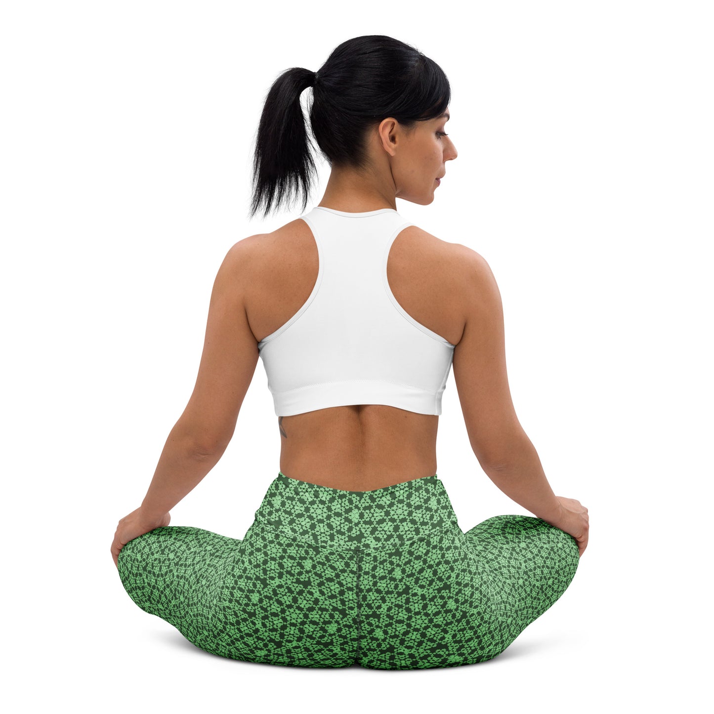 Back shot of a young woman sitting in lotus position wearing leggings with the 'Heptagon' green fractal geometric pattern.