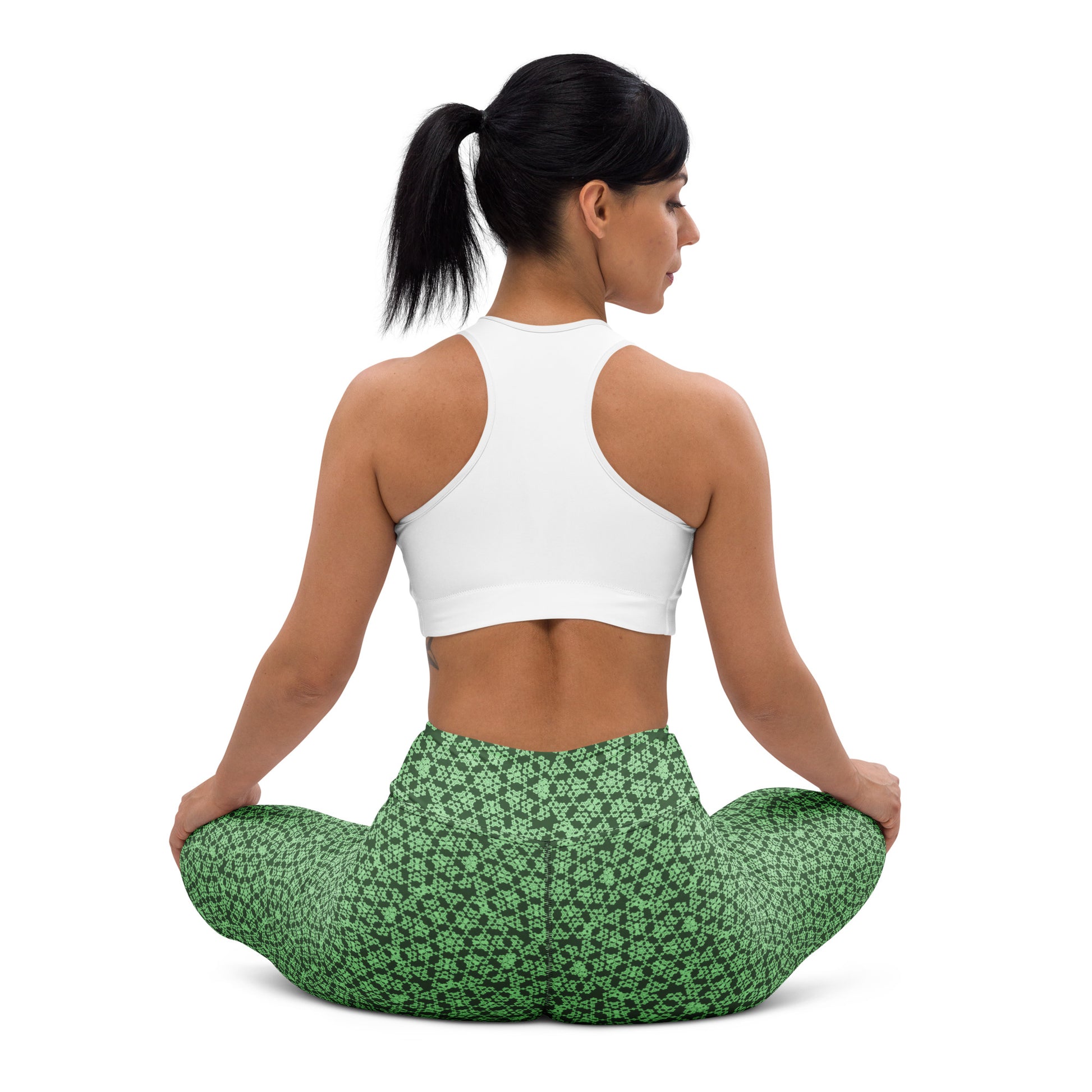 Back shot of a young woman sitting in lotus position wearing leggings with the 'Heptagon' green fractal geometric pattern.