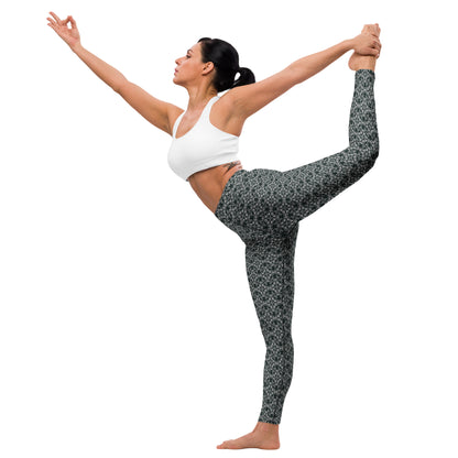 Young woman in a yoga pose wearing leggings with the 'Quadragon' charcoal and white fractal geometric pattern.