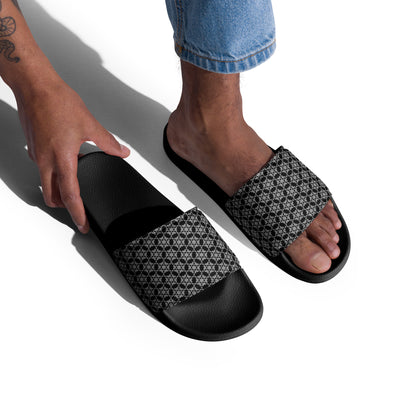 Foot in one of the 'Hexagon' black and white fractal geometric pattern men's slides while a hand reaches for the other, on a white background.