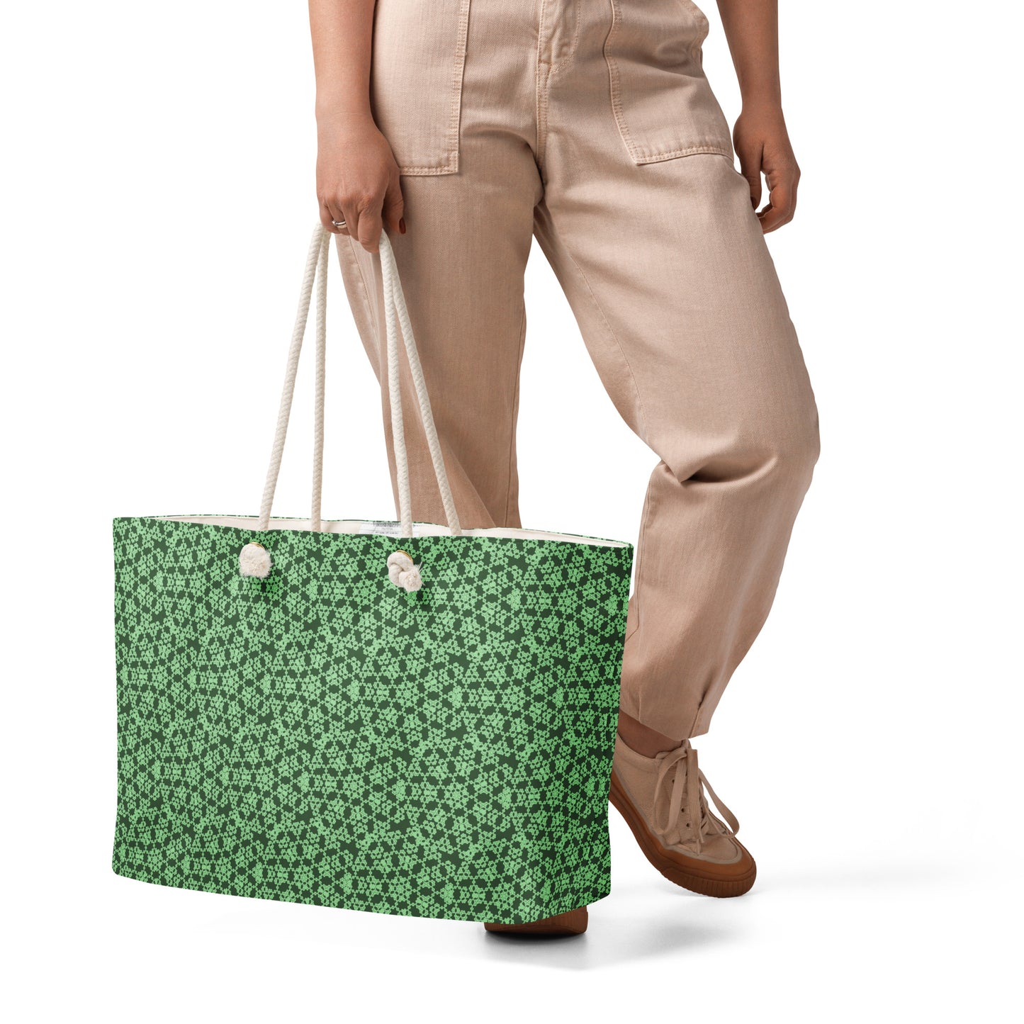 Close up of the lower part of a model holding the oversized weekender bag with the 'Heptagon' green fractal geometric pattern.